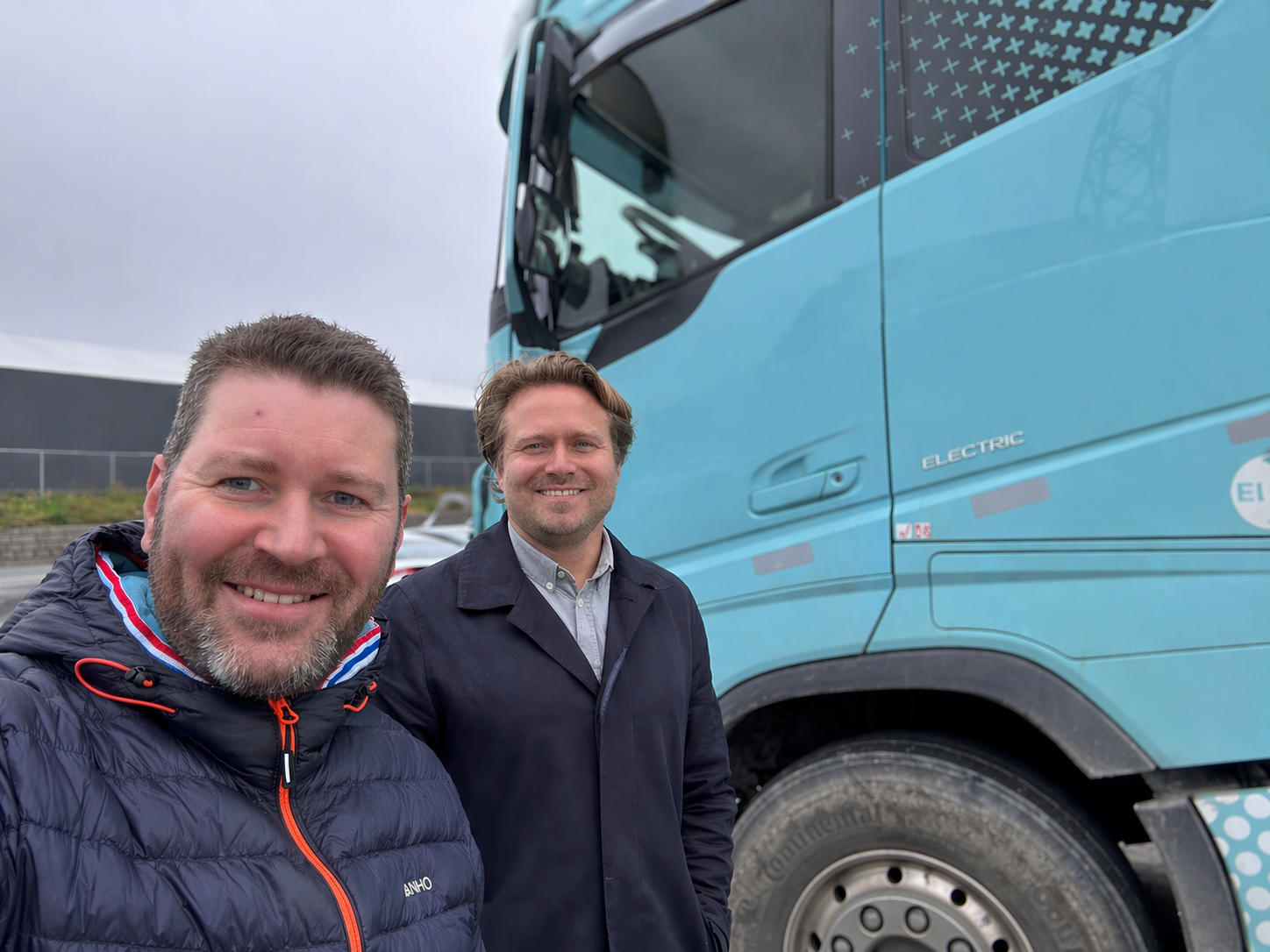 To smilende menn står foran en lyseblå elektrisk semitrailer.