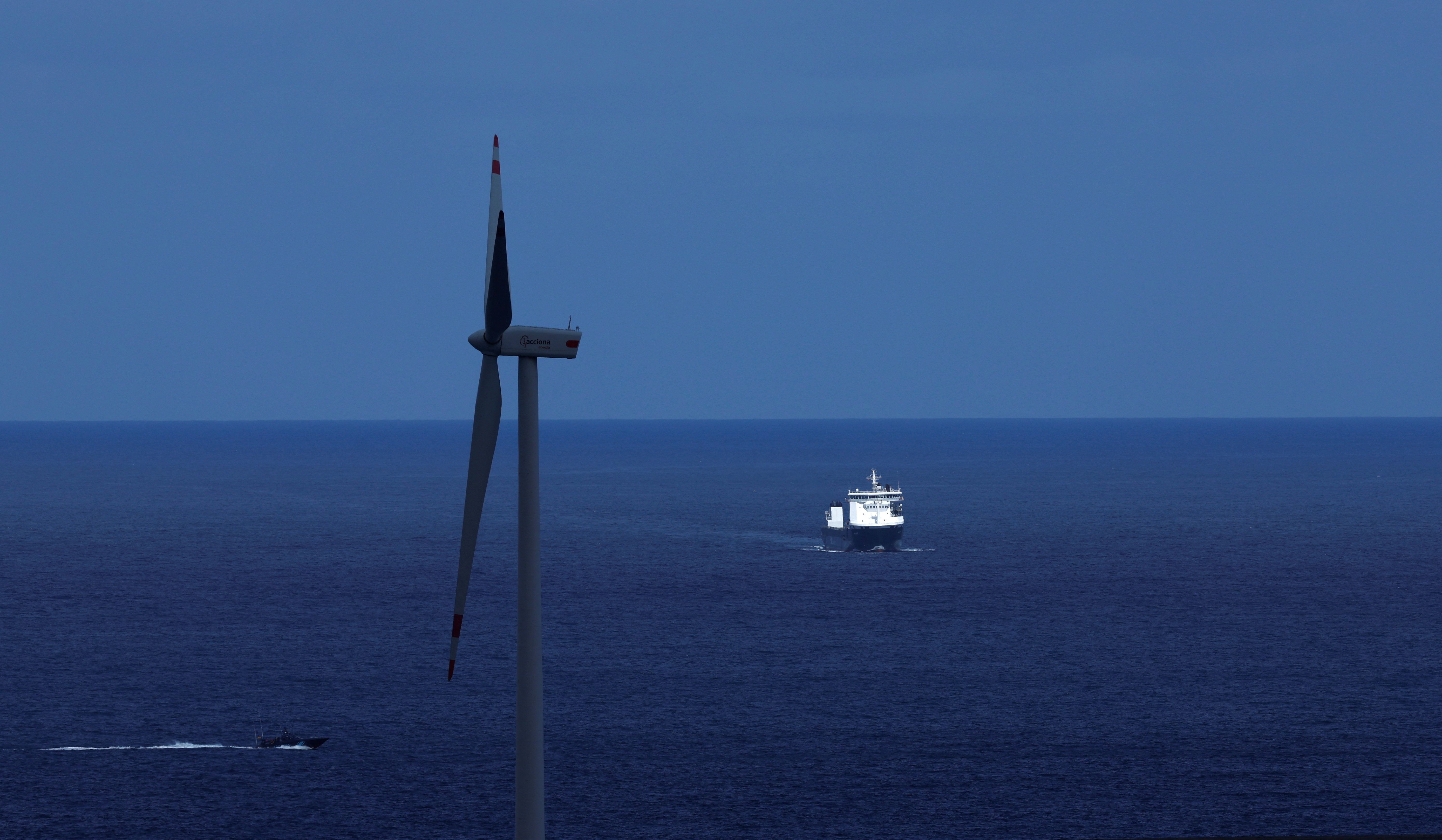 Havvindturbin, stort skip og mørk ubåt på et mørkeblått hav.