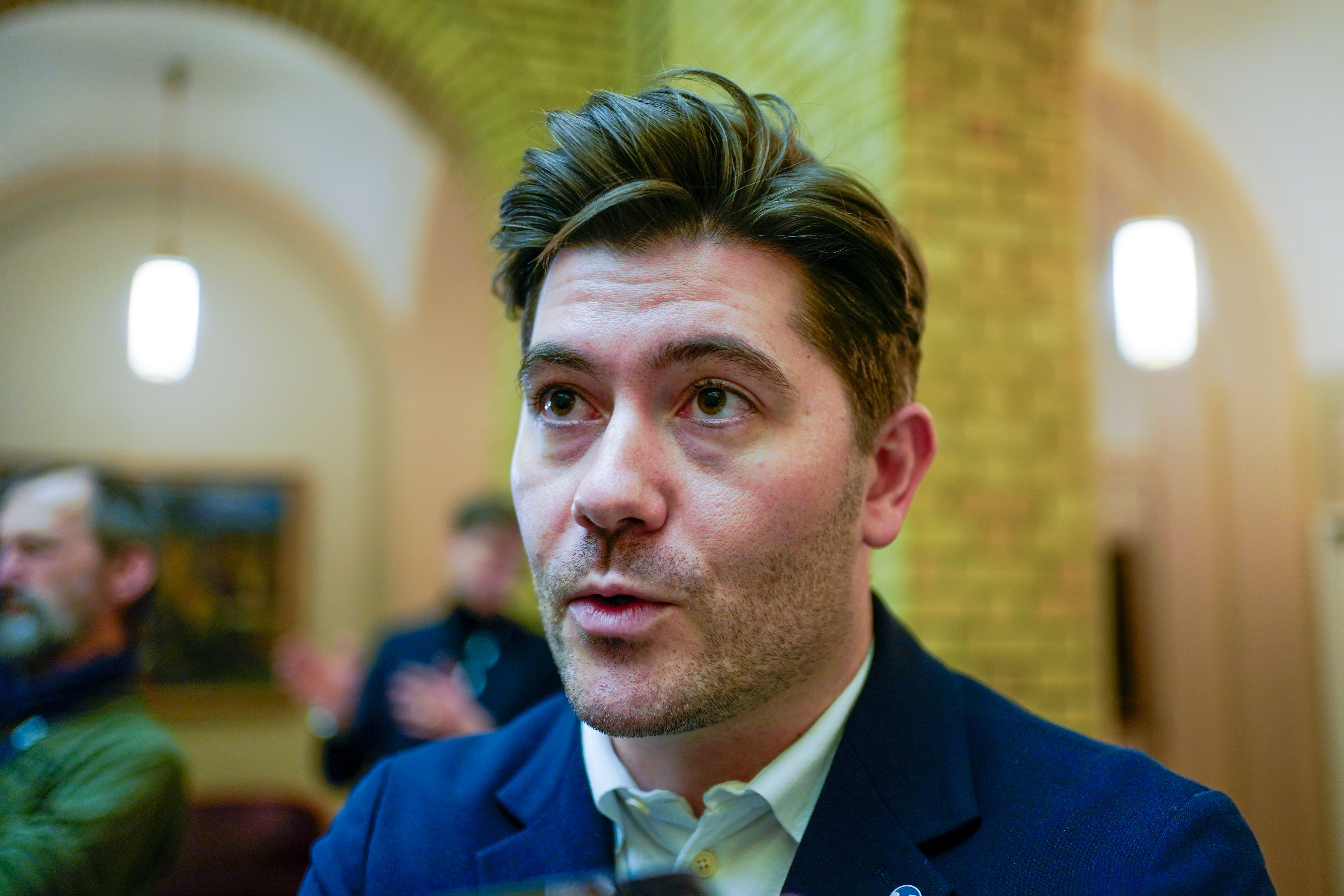 En mann med mørkt hår og skjegg snakker og ser litt oppover.