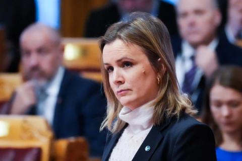 En kvinne med alvorlig mine, iført en lys høyhalset genser og en mørk blazer, i stortingssalen med uskarpe personer i bakgrunnen.