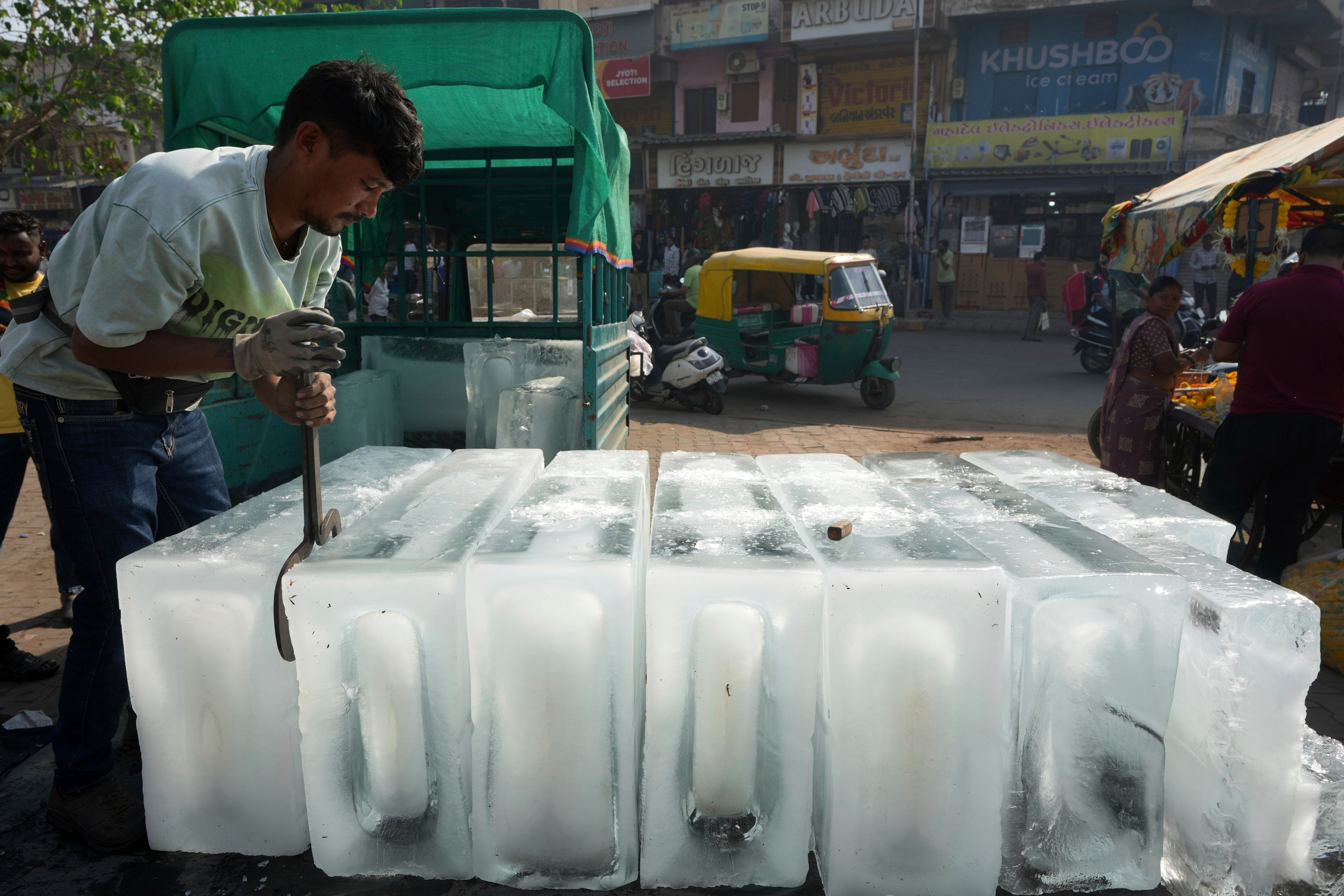 En mann bruker en ishakke til å flytte store isblokker i en solfylt gate.