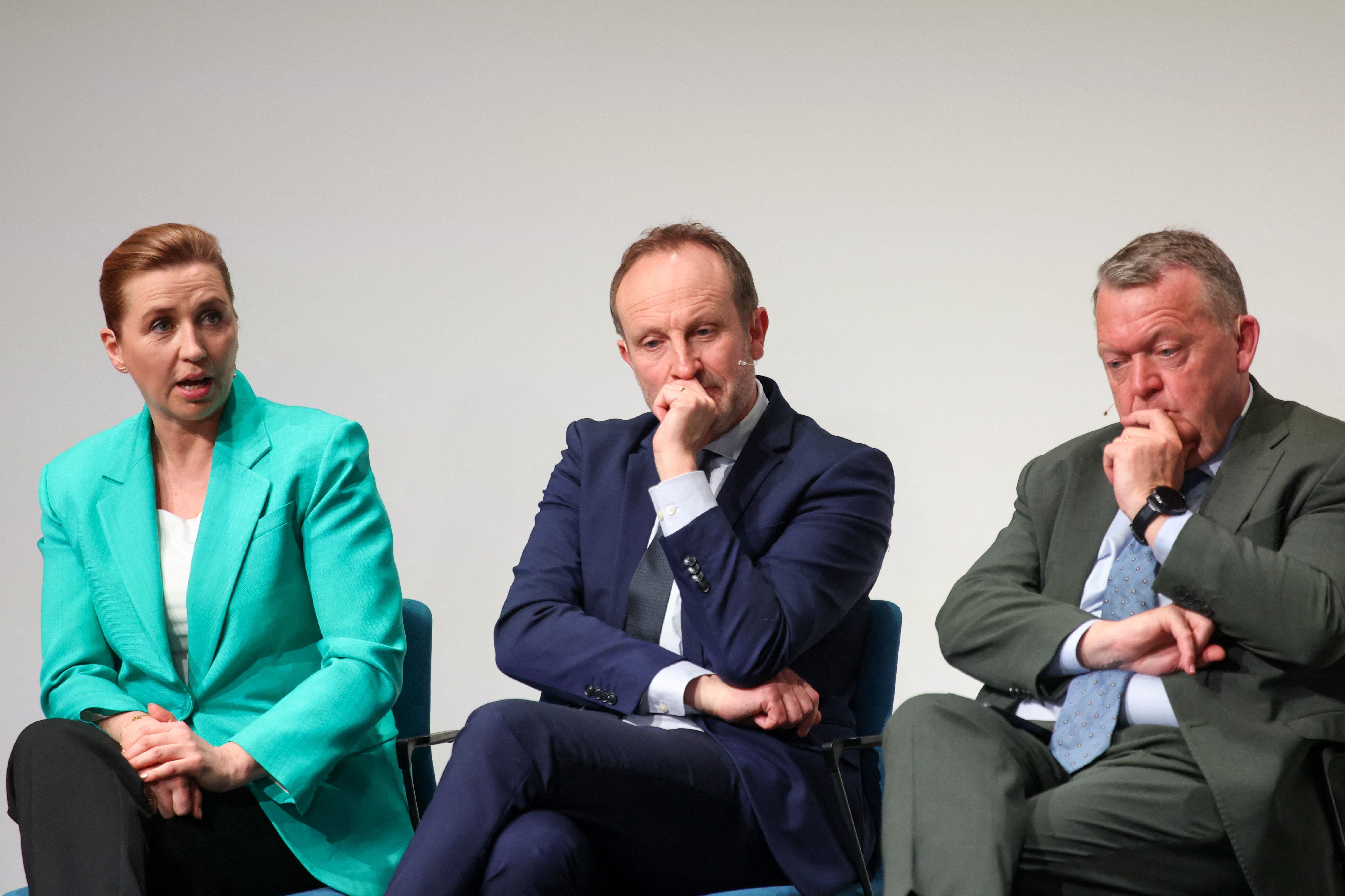 En kvinne i turkis blazer og to menn i dress sitter med ettertenksomme uttrykk.