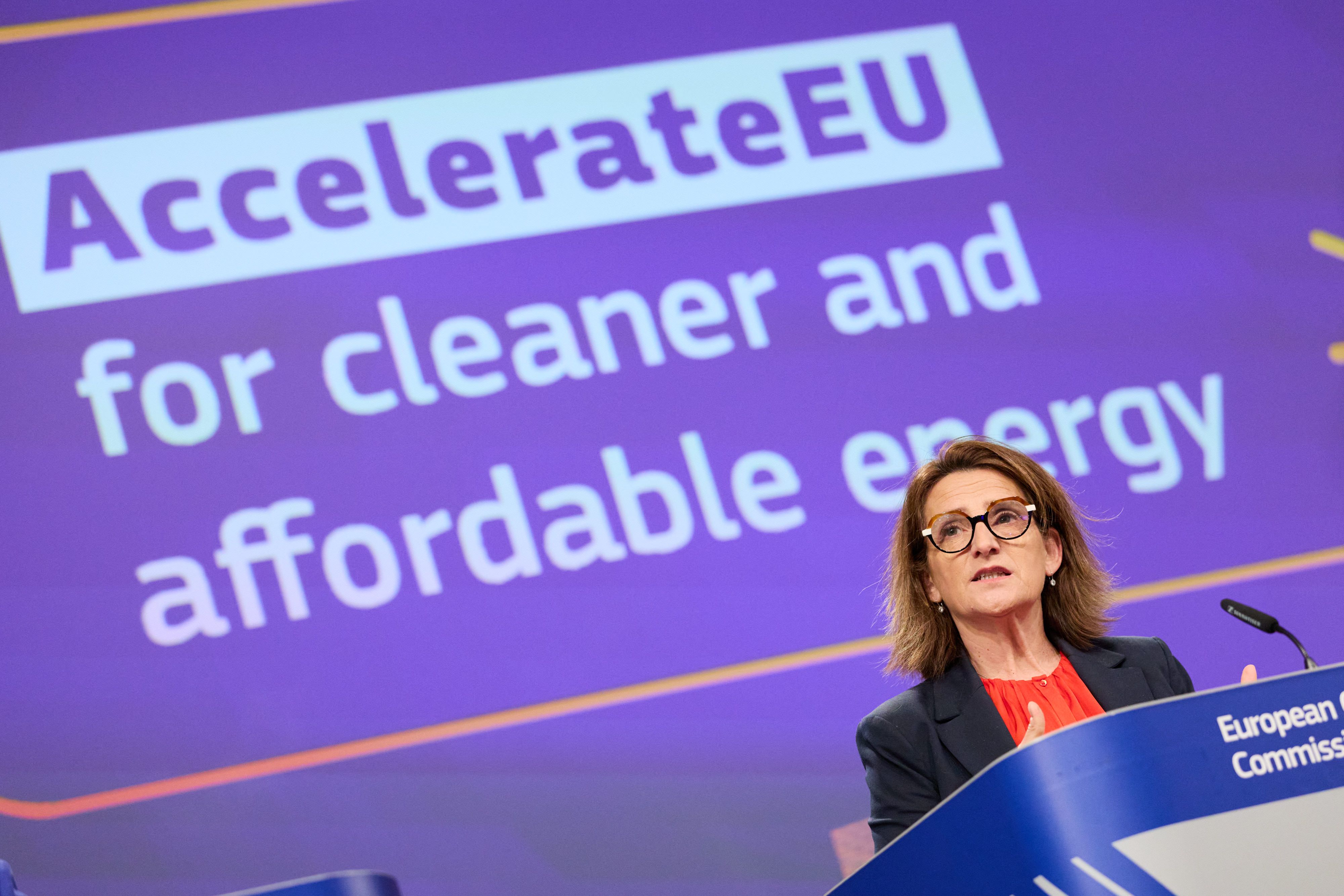 En kvinne taler fra en talerstol foran en lilla skjerm med teksten «AccelerateEU for cleaner and affordable energy.»