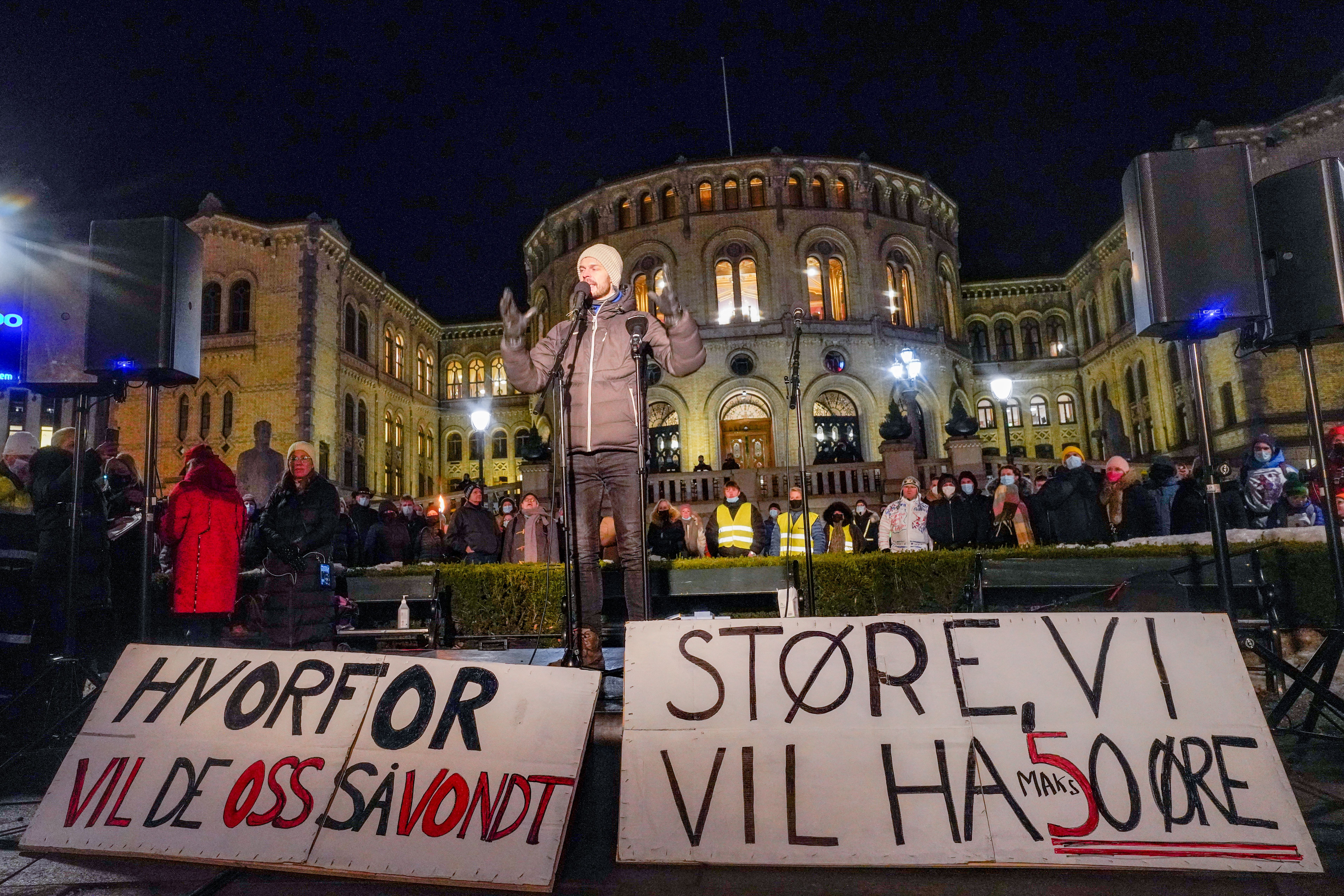 En mann holder en appell utenfor Stortinget, med to norske protestplakater i forgrunnen. På plakatene står det: Hvorfor vil de oss så vondt? Og: Støre, vi vil ha 50 øre.