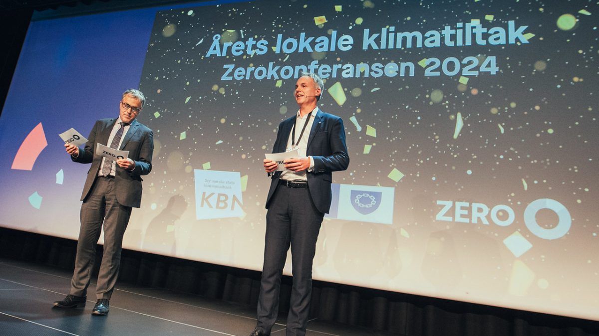 To menn i dress står på scenen med papirer i hendene på Zerokonferansen 2024-arrangementet, med en skjerm bak dem som viser "Årets lokale klimatiltak".