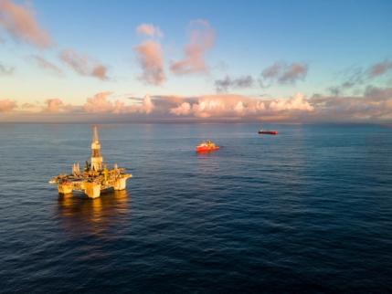Offshore oljeplattform med to skip til havs under en skyet himmel.