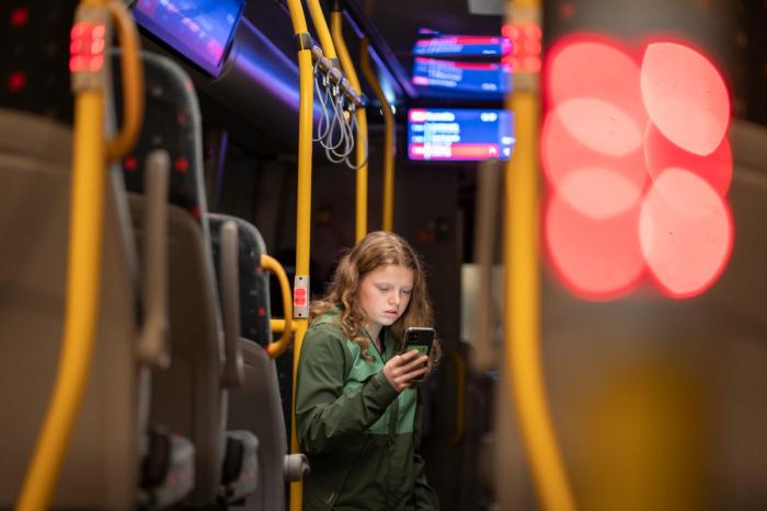 En ung jente ser på smarttelefonen sin inne i en buss.