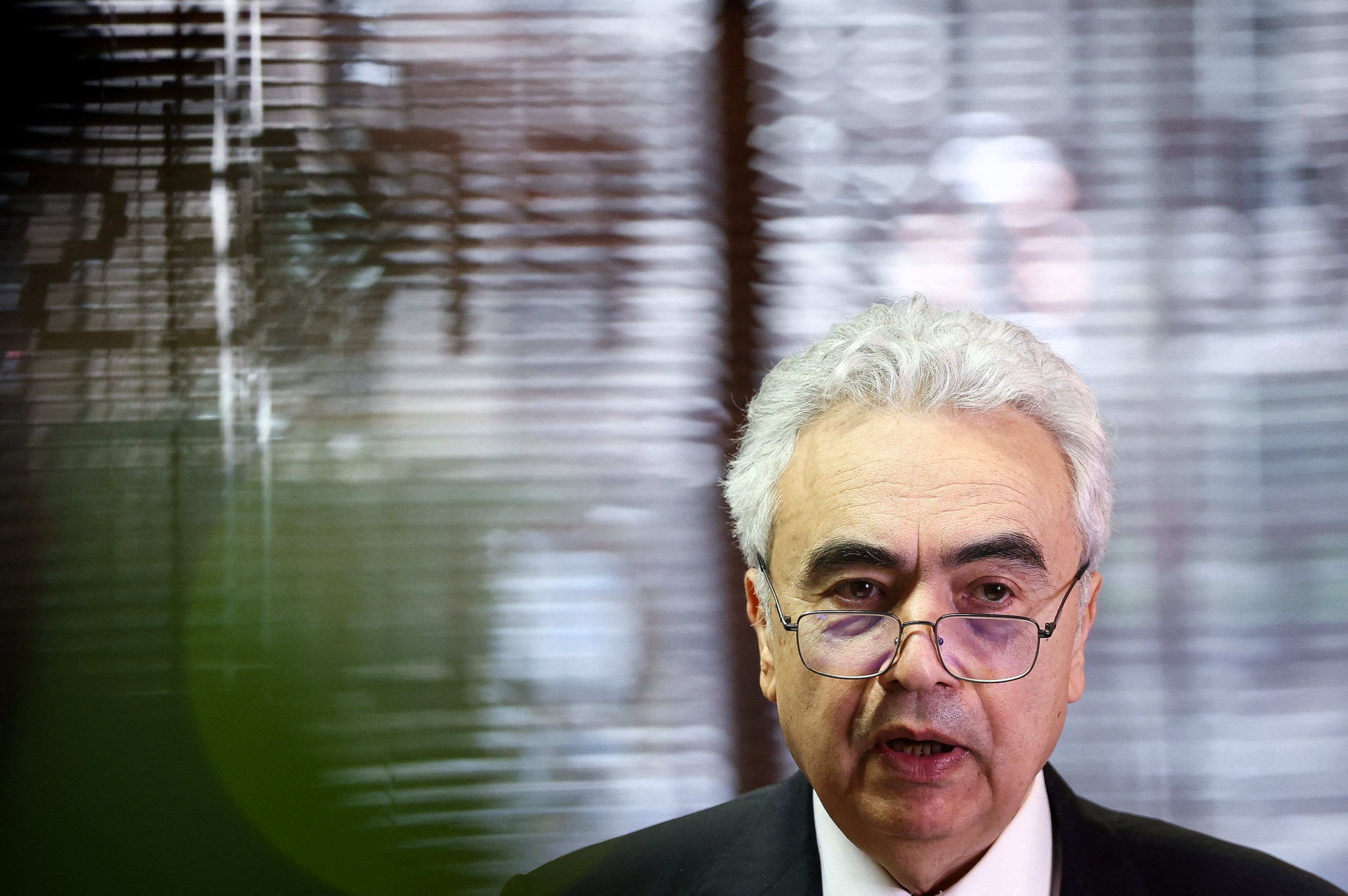 En mann med grått hår og briller, iført dress, snakker.