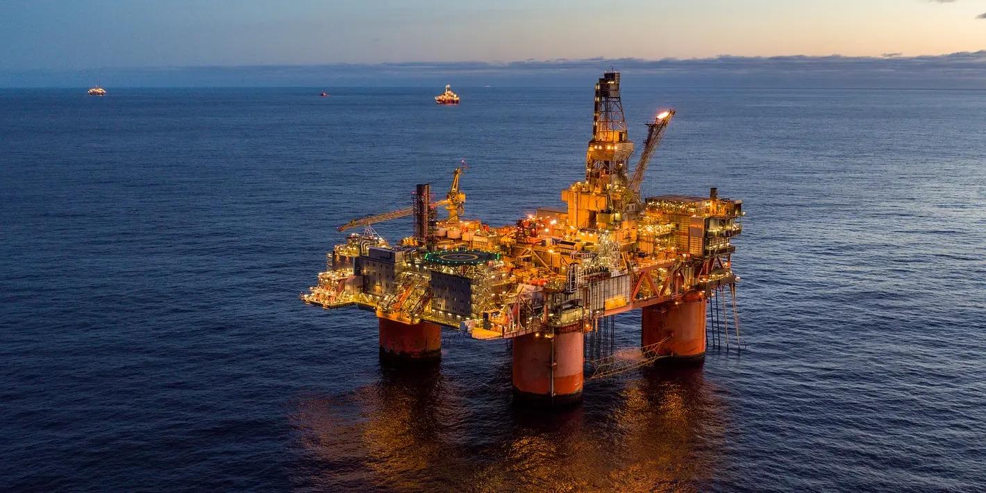 Offshore oil rig brightly lit at twilight with a flare burning.