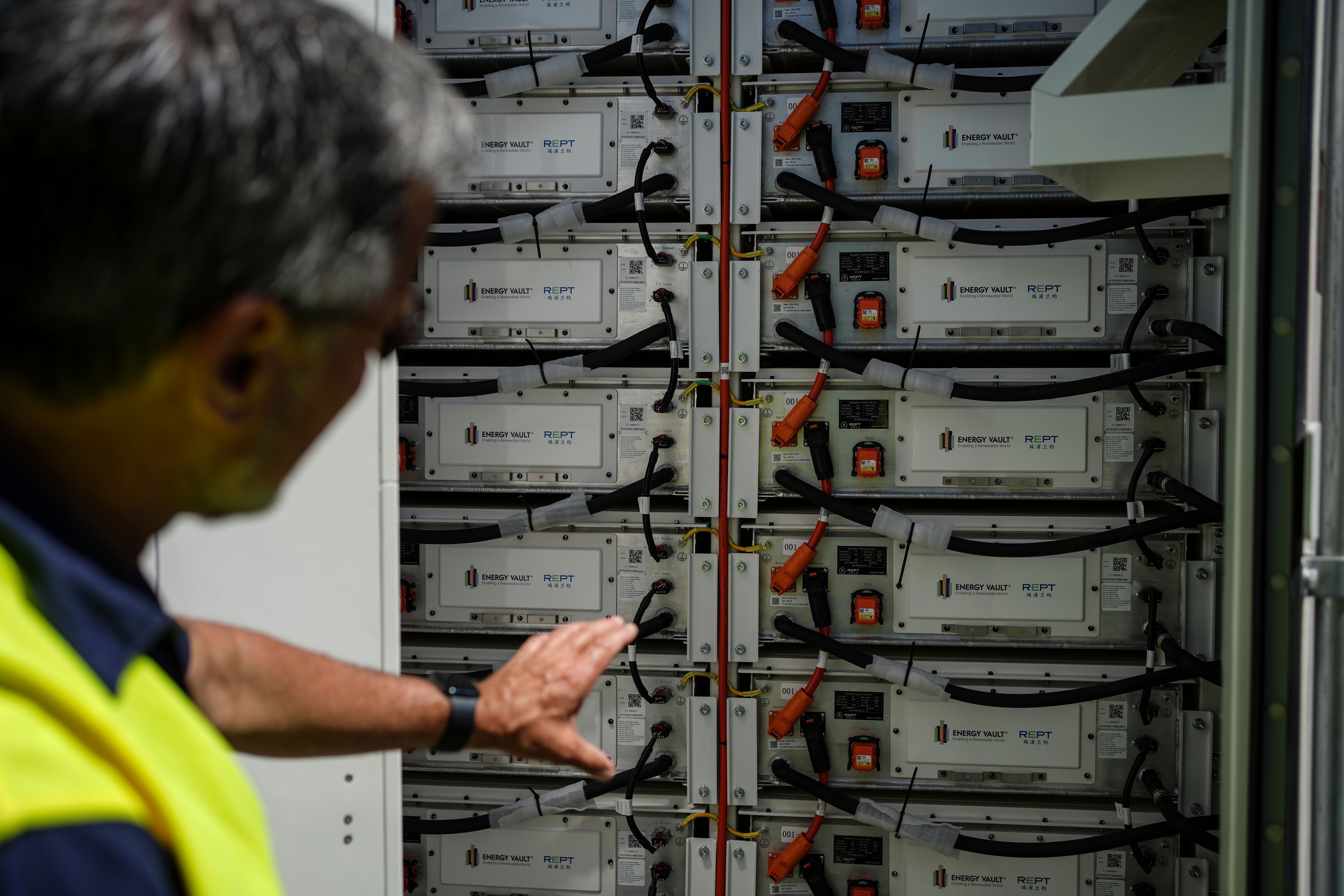 En person i en synlighetsvest inspiserer et stativ med industrielle batterier.