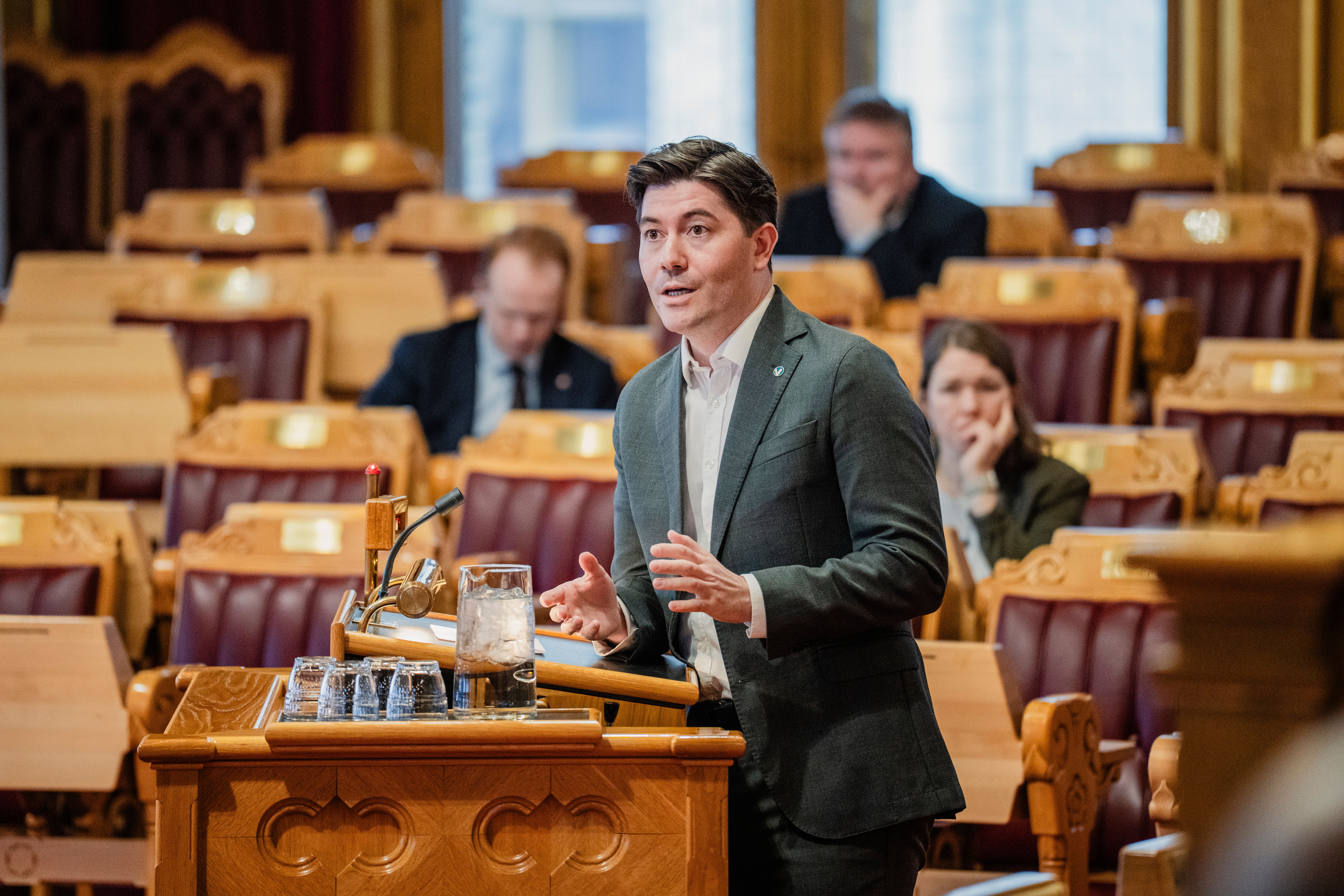 En mann i dress taler fra en talerstol i en lovgivende forsamling.