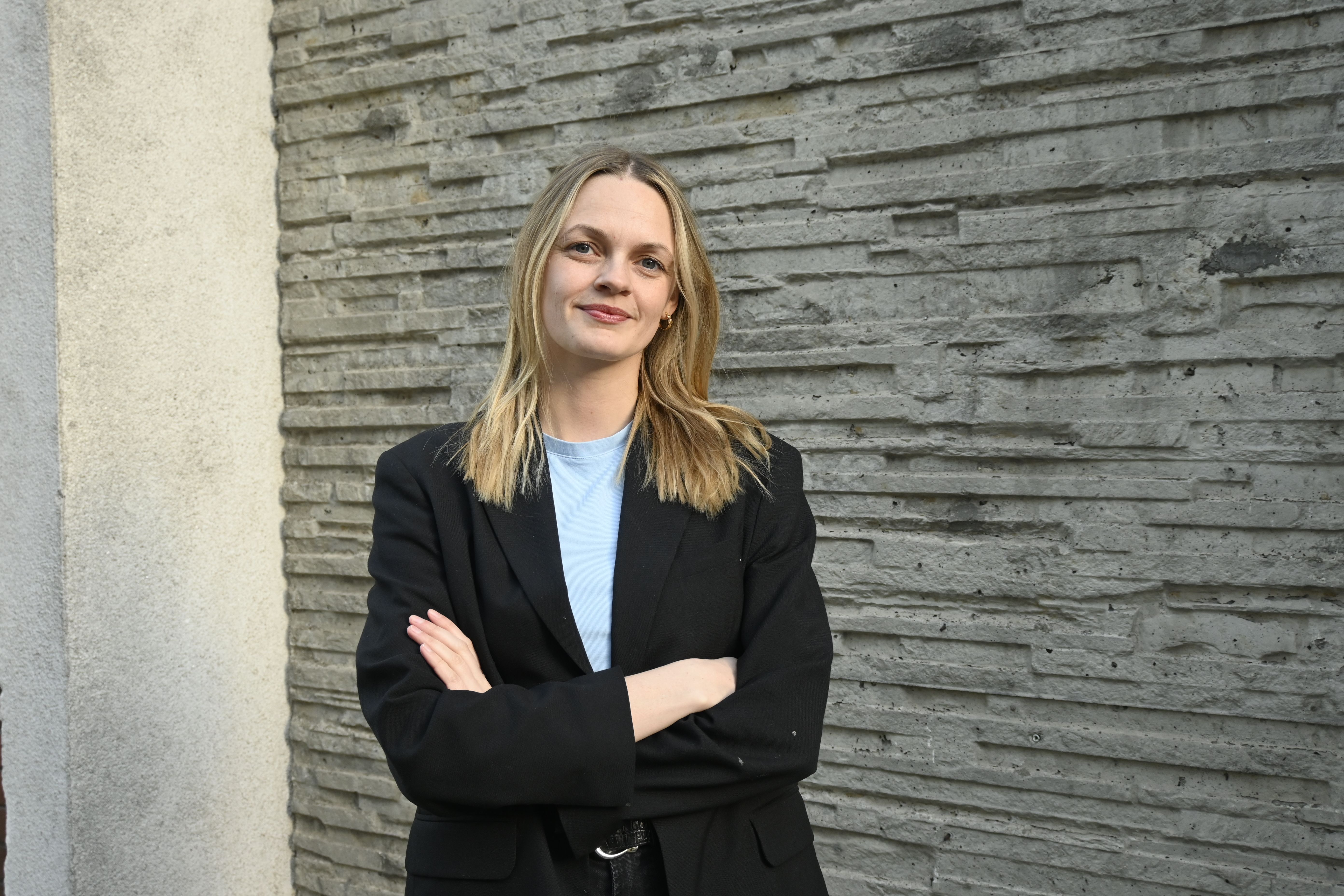 Fotografi av en kvinne som står selvsikkert foran en vegg.