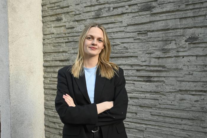 Fotografi av en kvinne som står selvsikkert foran en vegg.