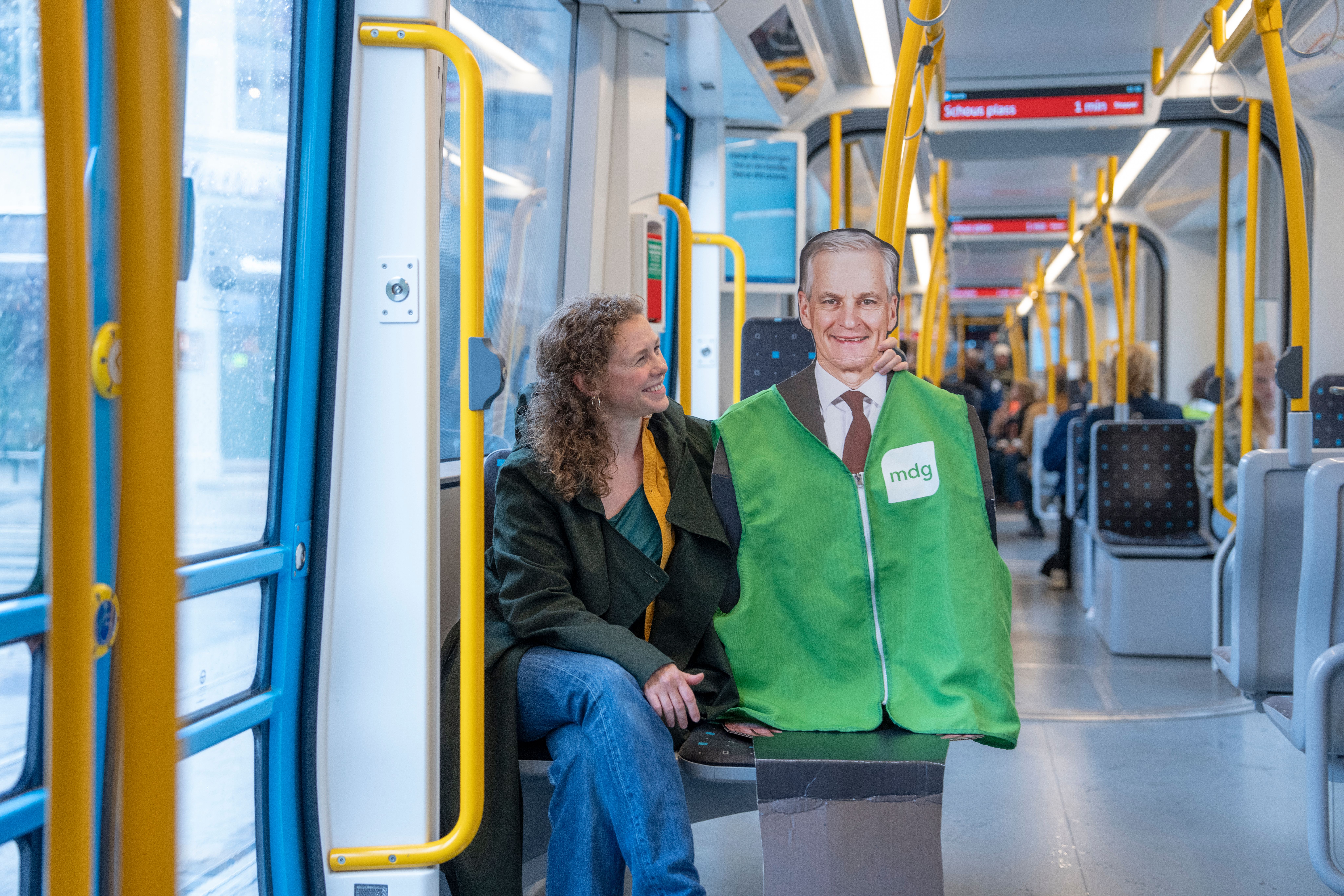 Bildet viser Ingrid Liland (MDG) på en trikk som smiler til en pappfigur av Jonas Gahr Støre i grønn «mdg»-vest.