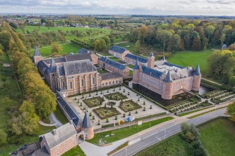 Flyfoto av et historisk anlegg med en vollgravsomkranset borg, formelle hager og en stor klosterbygning, omgitt av grønne jorder.