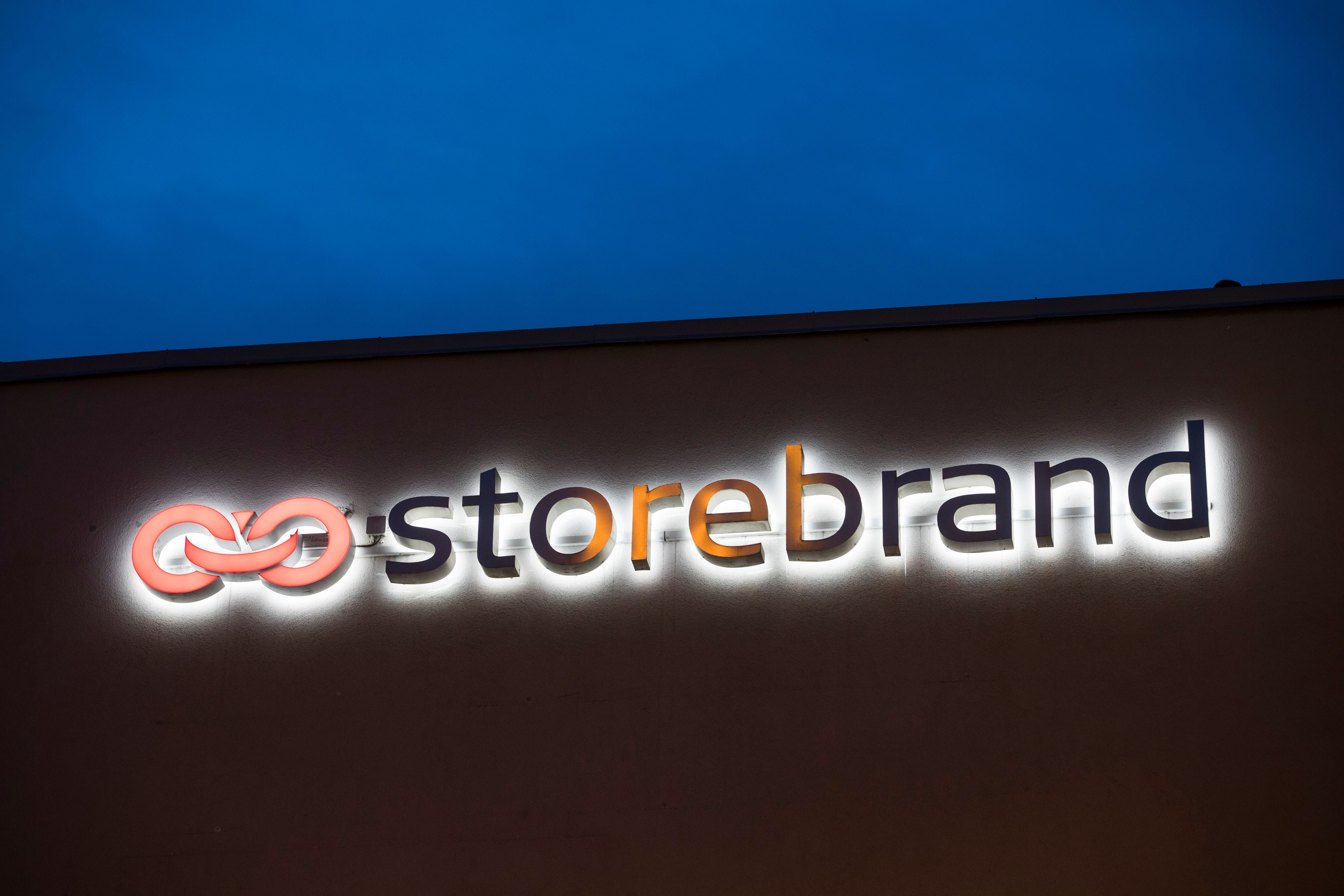 Opplyst Storebrand-skilt med en oransje sammenflettet logo på en bygning om natten.