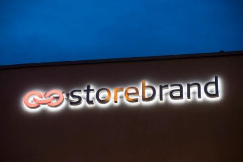 Opplyst Storebrand-skilt med en oransje sammenflettet logo på en bygning om natten.