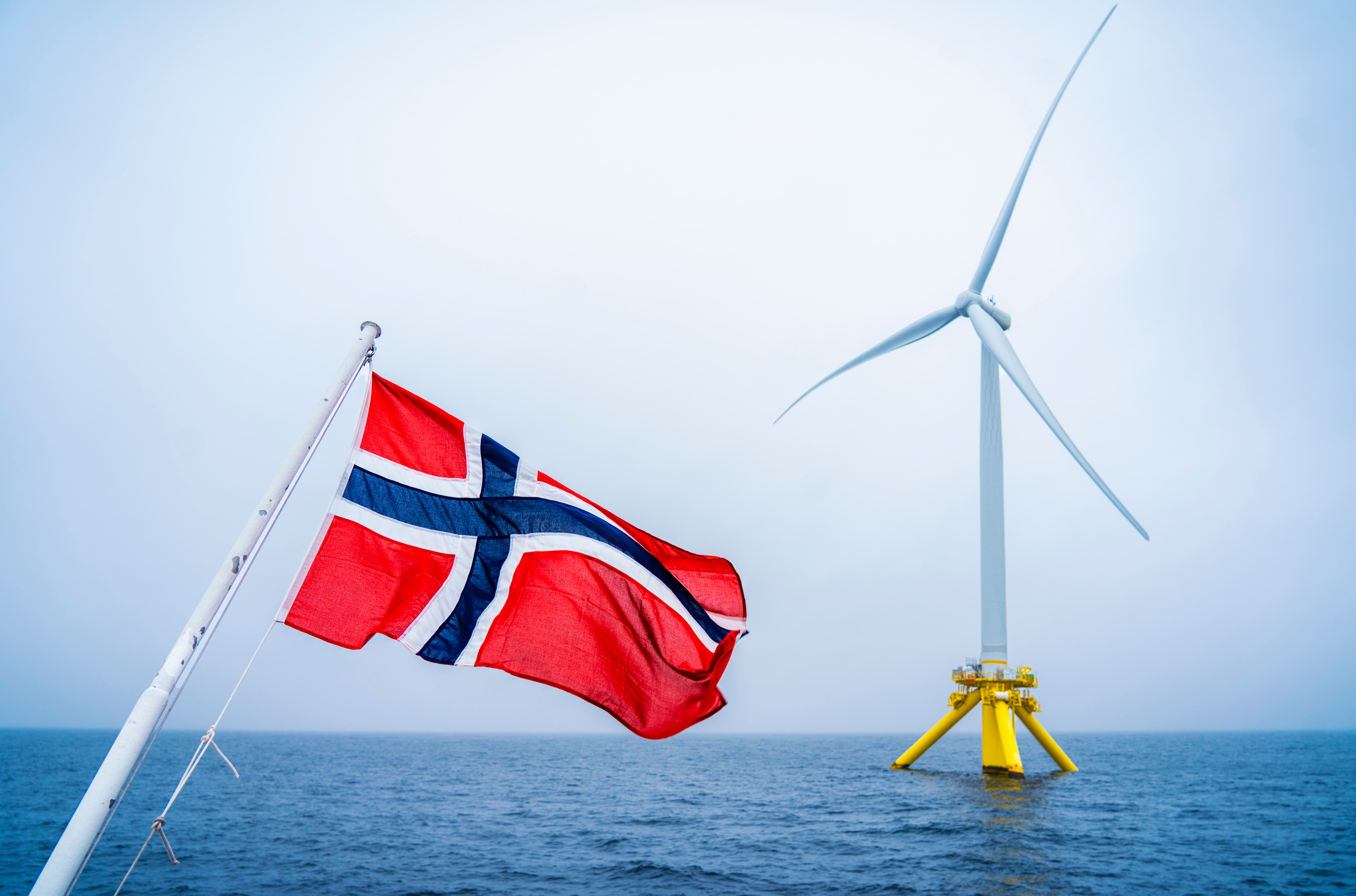 Norsk flagg som vaier fra en båt, med en havvindturbin ute i sjøen.
