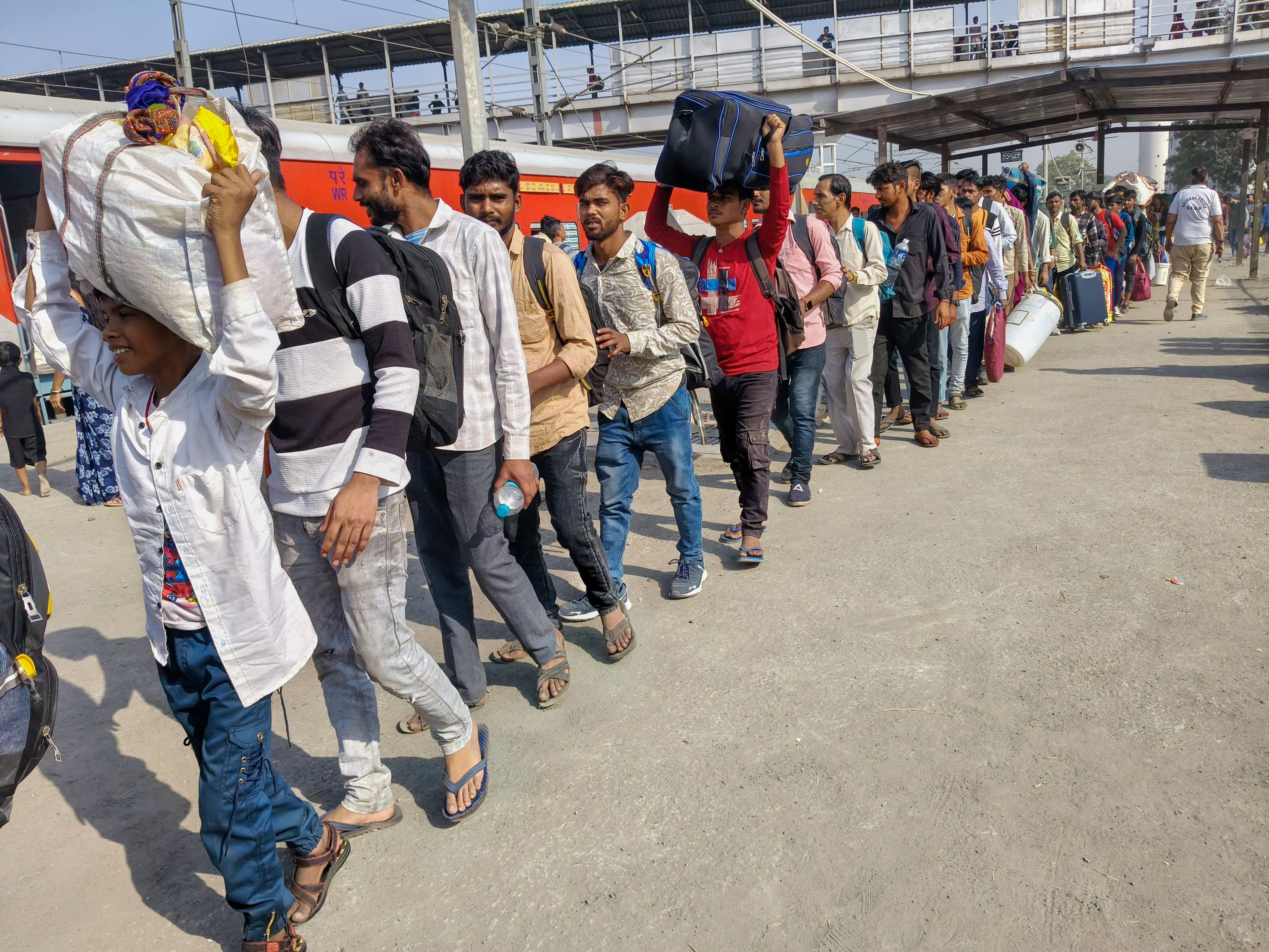 Long line of people carrying luggage on a train platform.