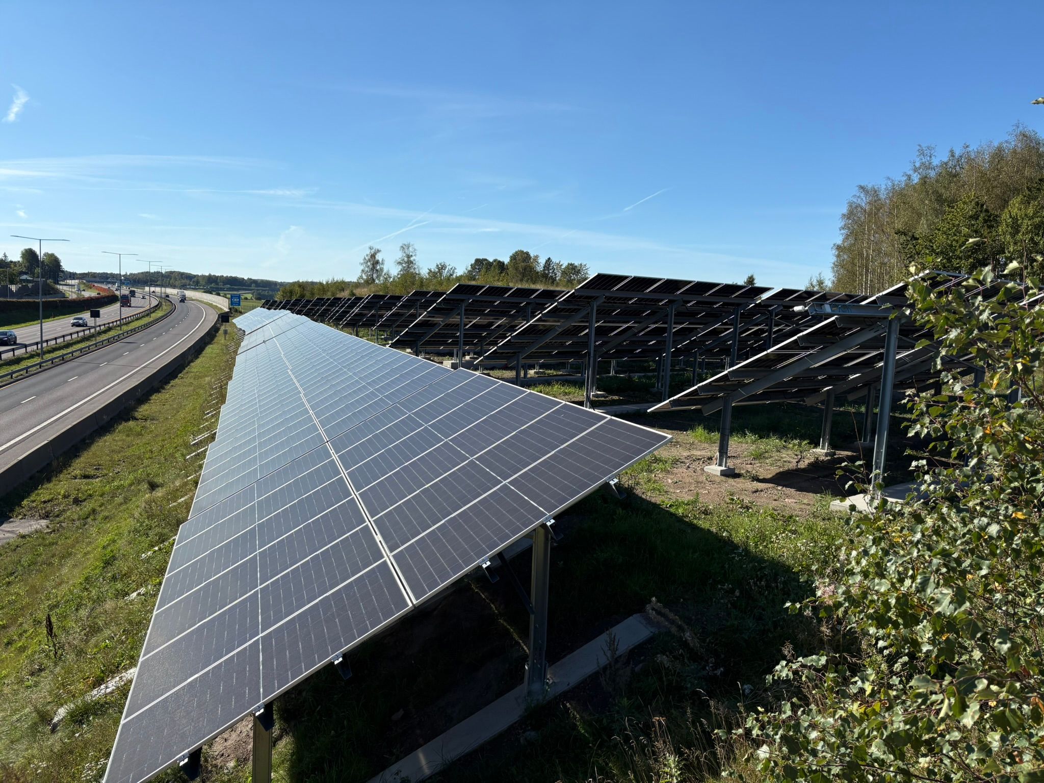 Solcellepaneler langs en motorvei under en klar blå himmel.