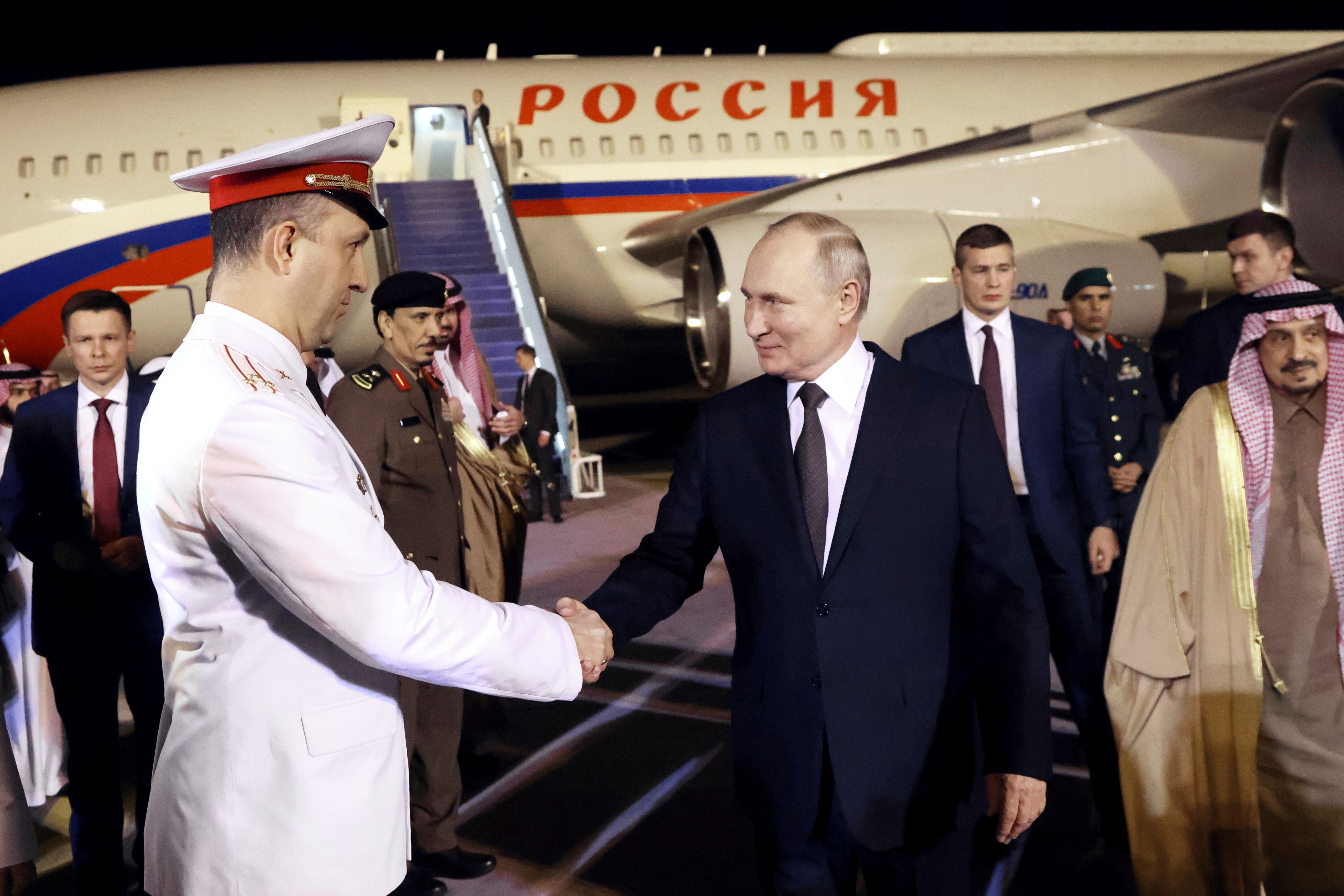 Russlands president Vladimir Putin håndhilser på en offiser på en flyplassrampe, med et russisk fly og saudiarabiske dignitærer i bakgrunnen.
