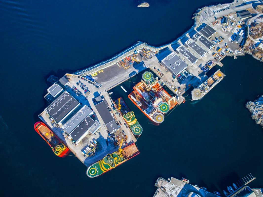 Flyfoto av en industrihavn med store skip, mange med helikopterdekk, fortøyd langs bygninger.