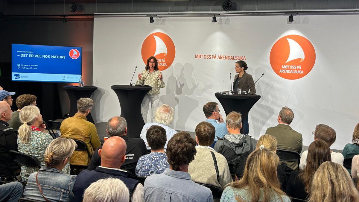 En foredragsholder henvender seg til et publikum på et innendørsarrangement med bakteppet "Møt oss på Arendalsuka." En annen person står i nærheten på et podium. En skjerm viser teksten "DE ER VEL NOK NATUR?.