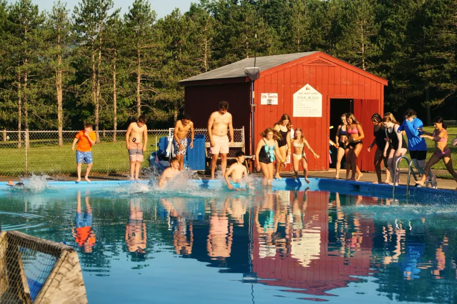 Campers jump into the bright blue camp pool on a sunny day