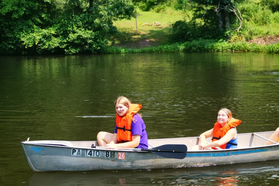 Two girls in life vests paddling a canoe on the lake