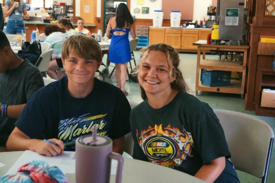 Two smiling teen campers sit side by side at a table in the dining hall