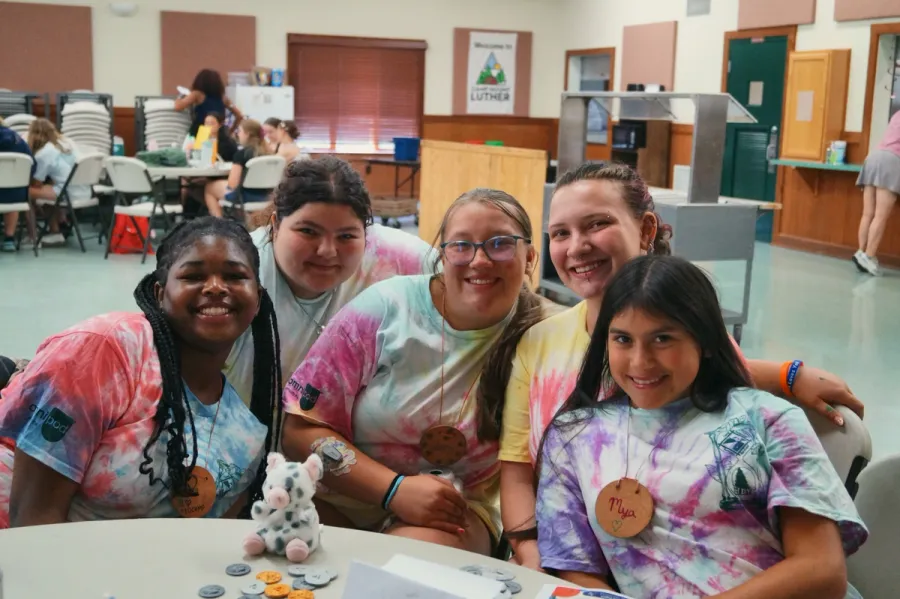 Five young campers in tie-dye shirts smile at the camera at a table