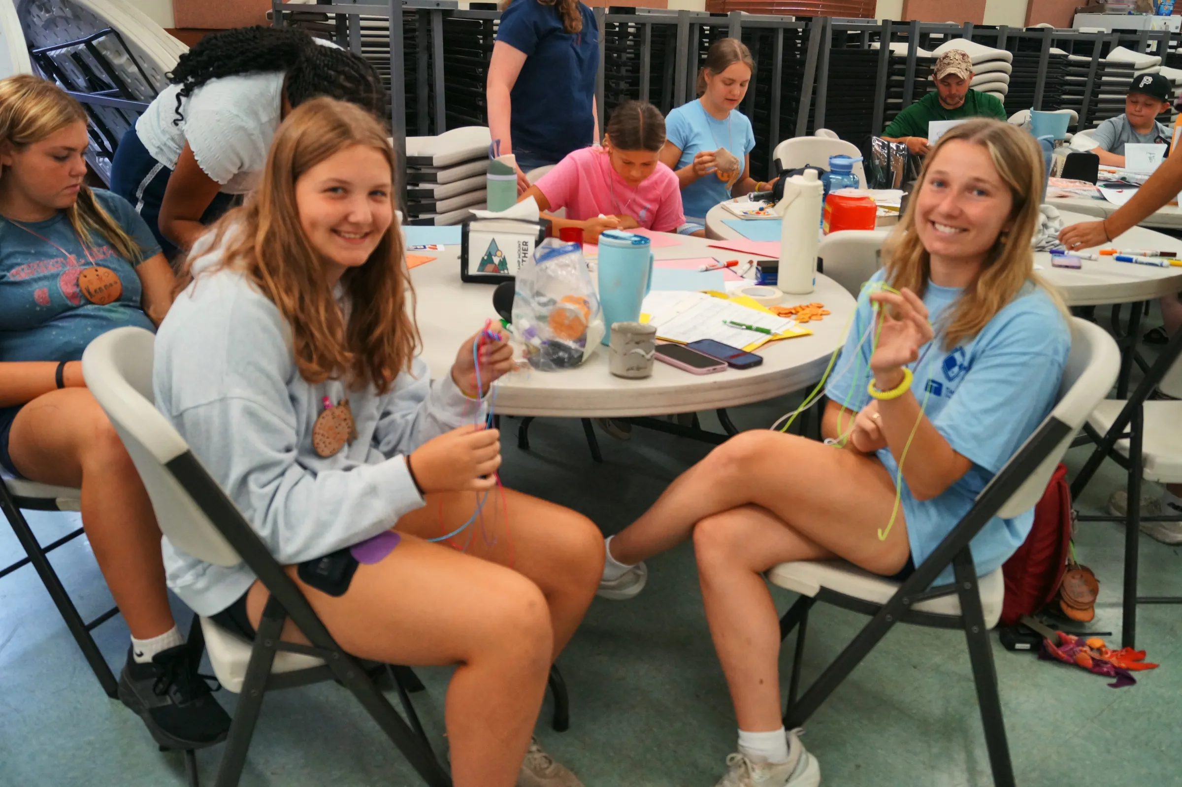 Two girls smiling as they make bracelets at the craft table