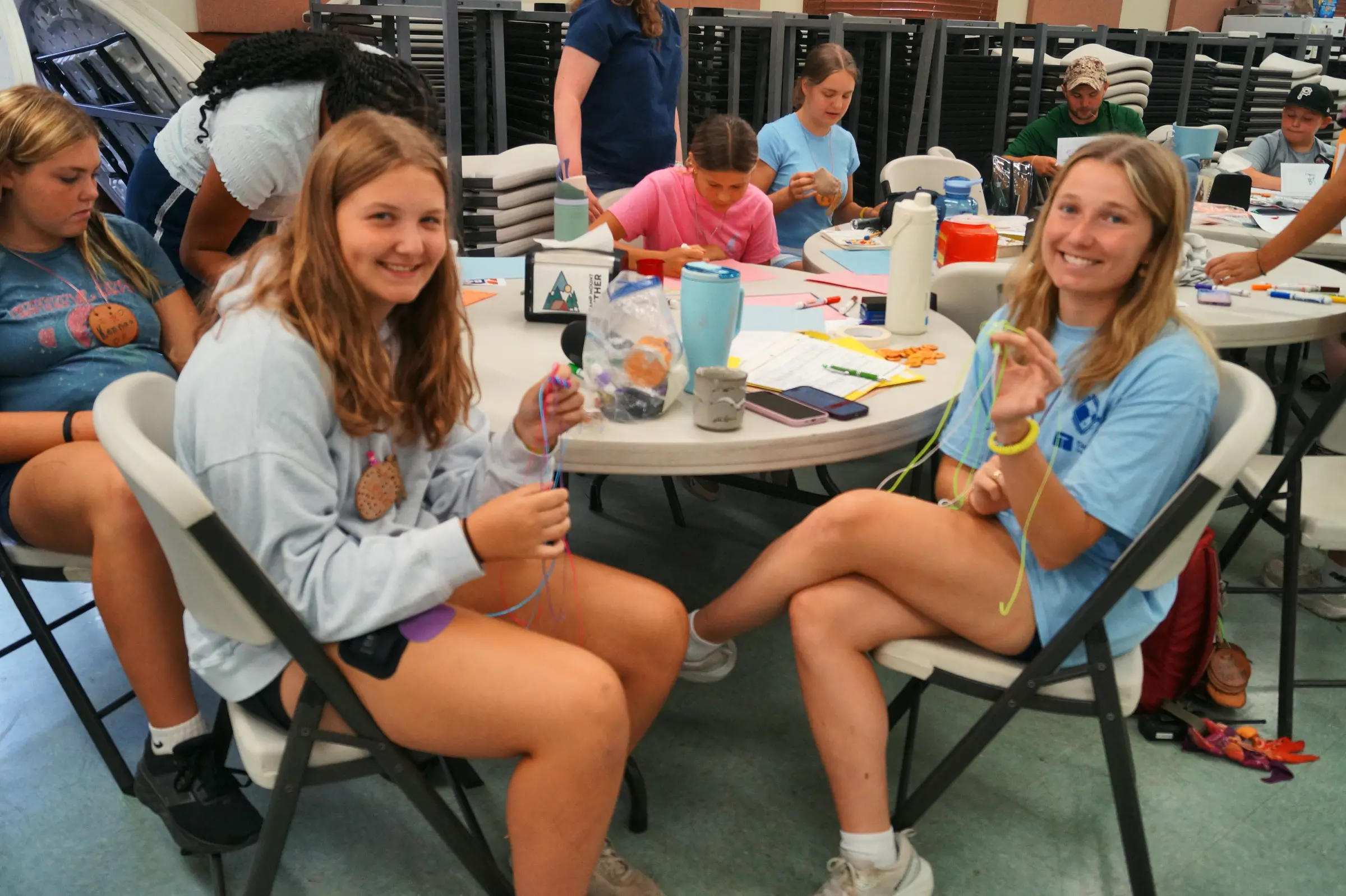 Two girls smiling as they make bracelets at the craft table
