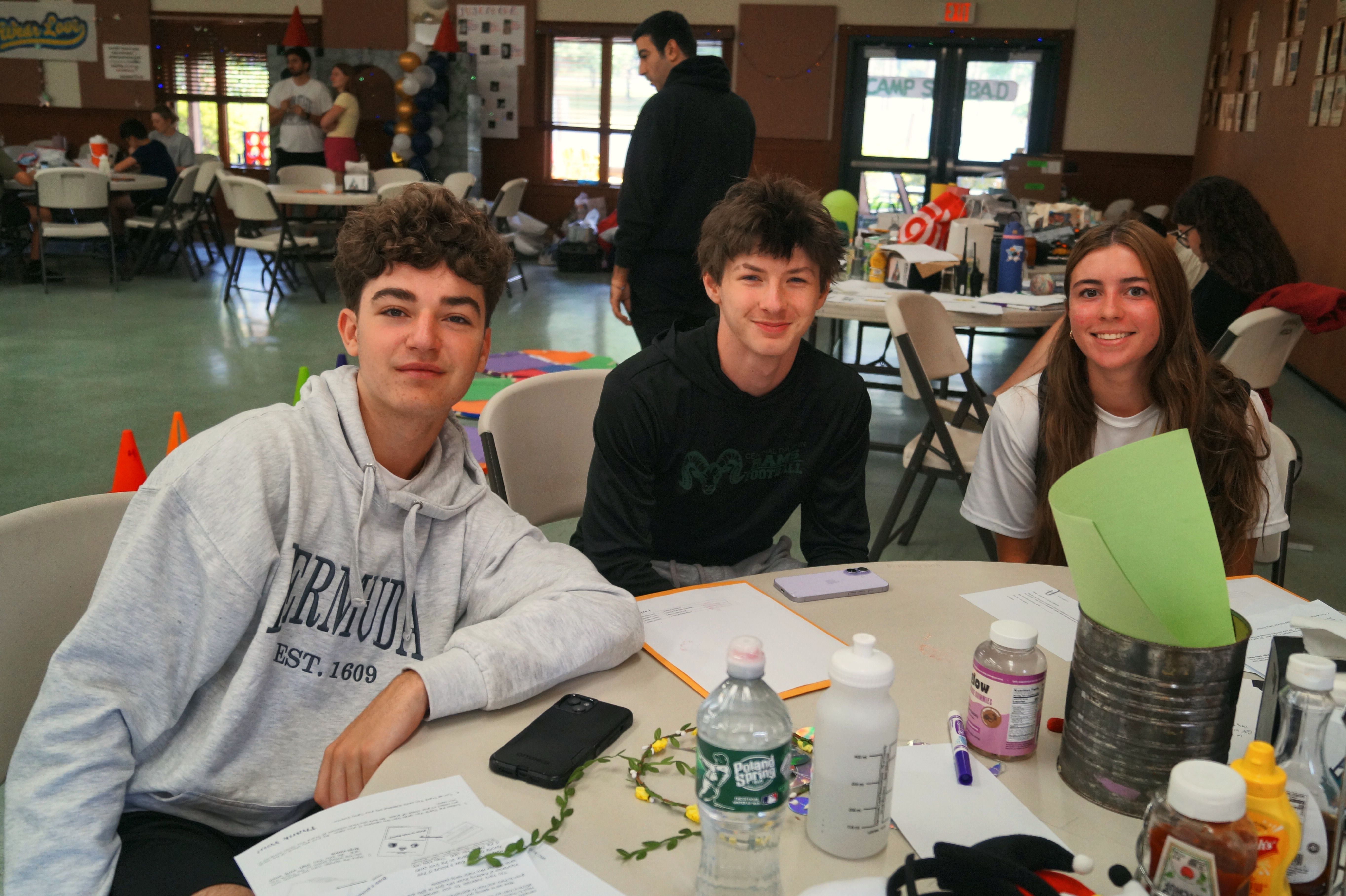 Three teen campers smile together at a table