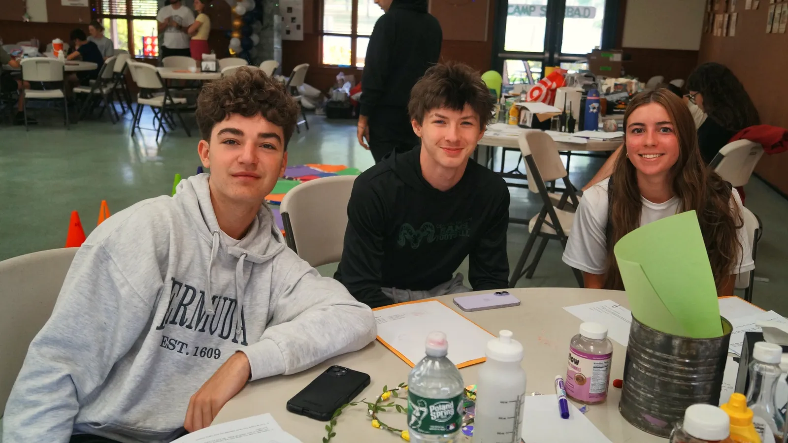 Three teen campers smile together at a table