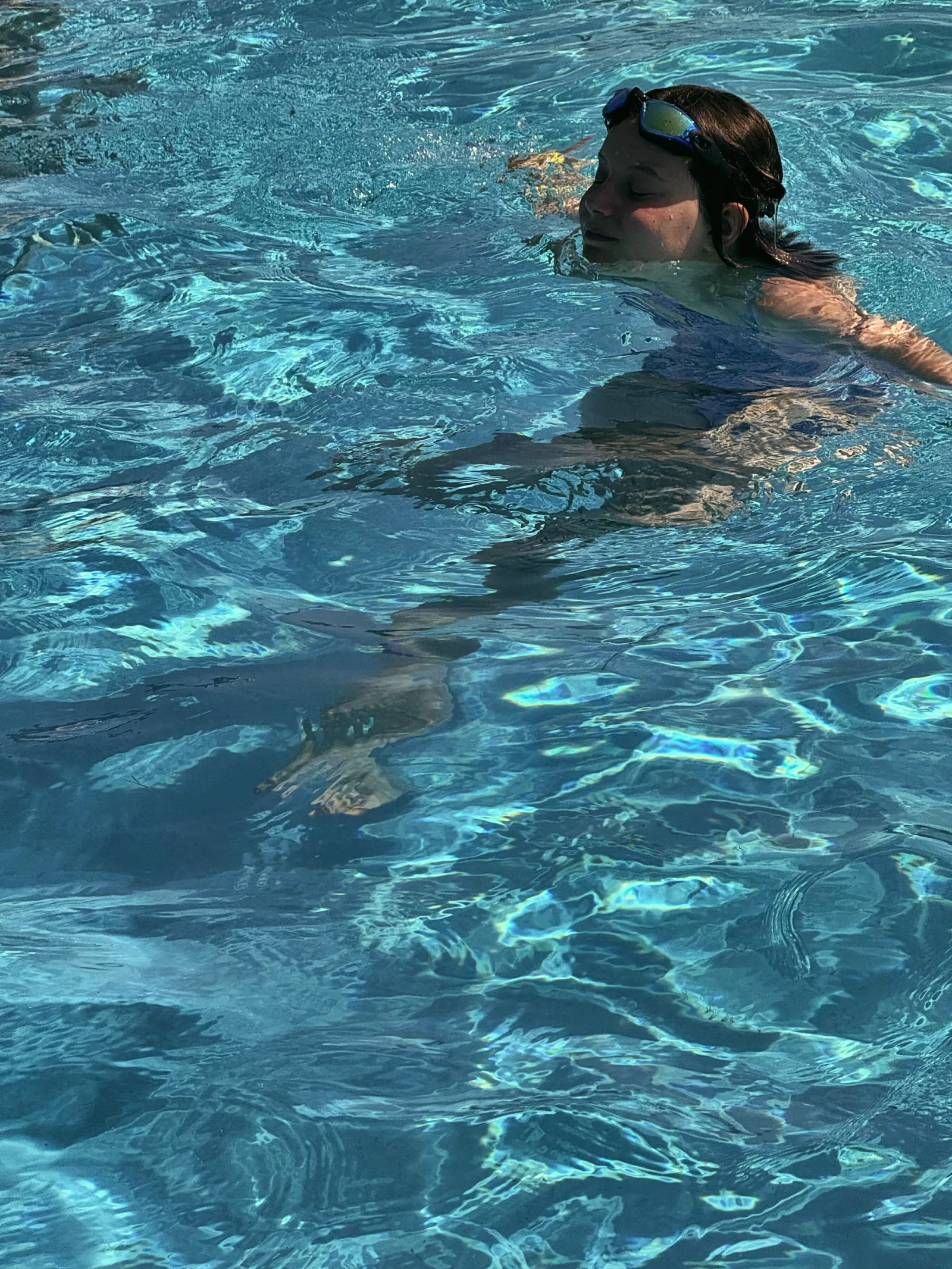 A girl with goggles on her head swims in the bright blue outdoor pool
