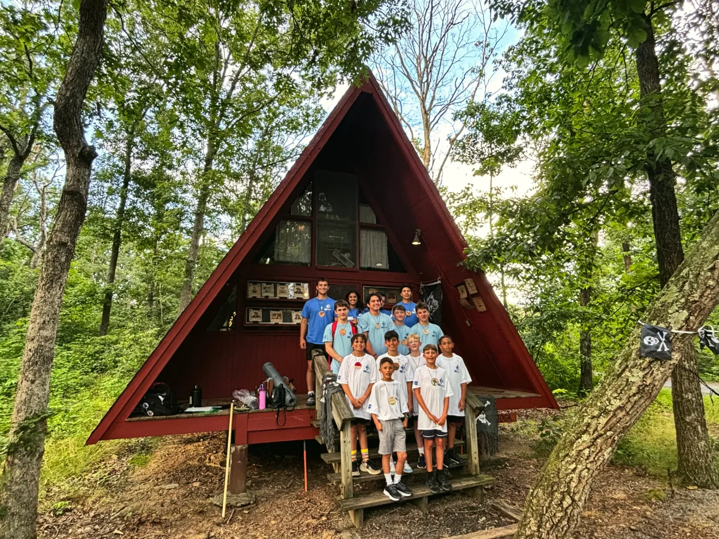 Campers and staff smiling on the steps of a red A-frame cabin