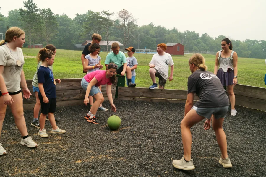Younger campers and teens play a ball game together in a gravel pit