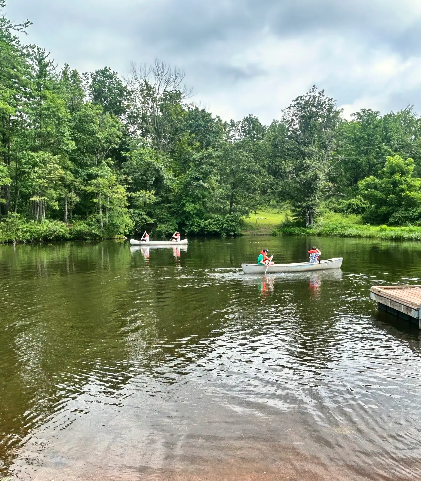 Canoes glide across a calm lake with a wooden dock, surrounded by trees.