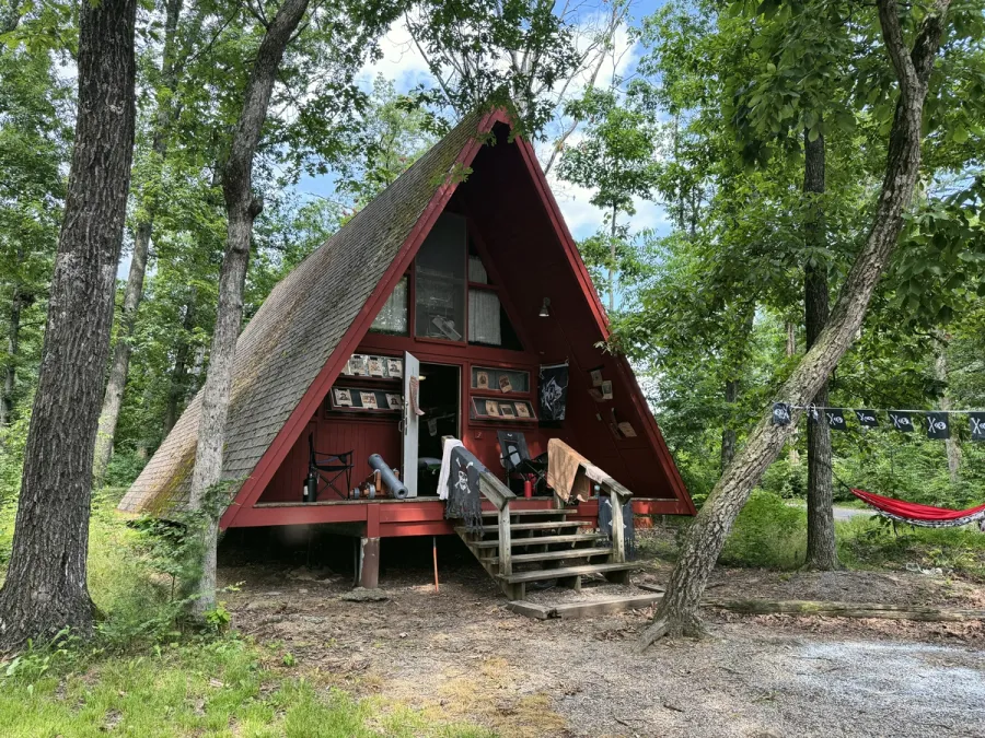 A red A-frame cabin among tall trees, with a red hammock beside the porch.