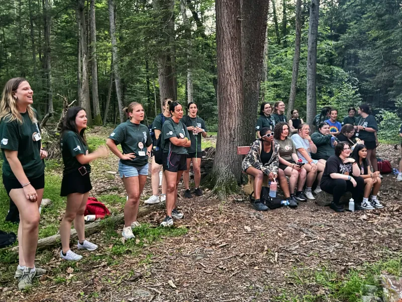 Young women in green camp shirts gathered in a forest clearing