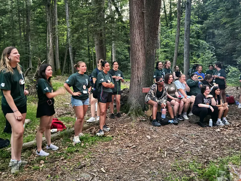 Young women in green camp shirts gathered in a forest clearing