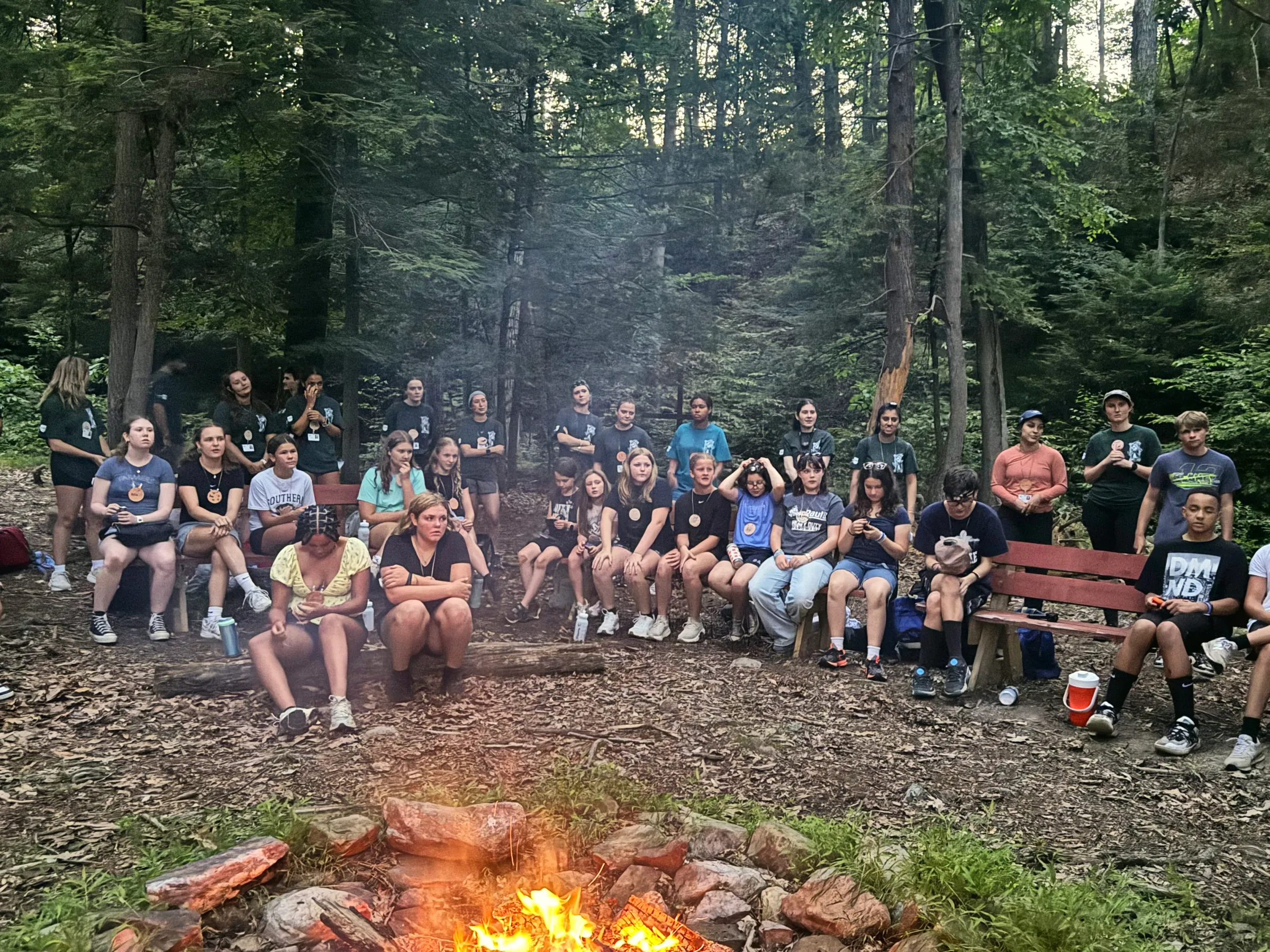 Campers and counselors gather around a campfire in the woods