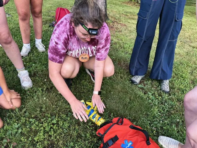 A staff member with a headlamp shows a group how to use a splint from a first-aid bag.