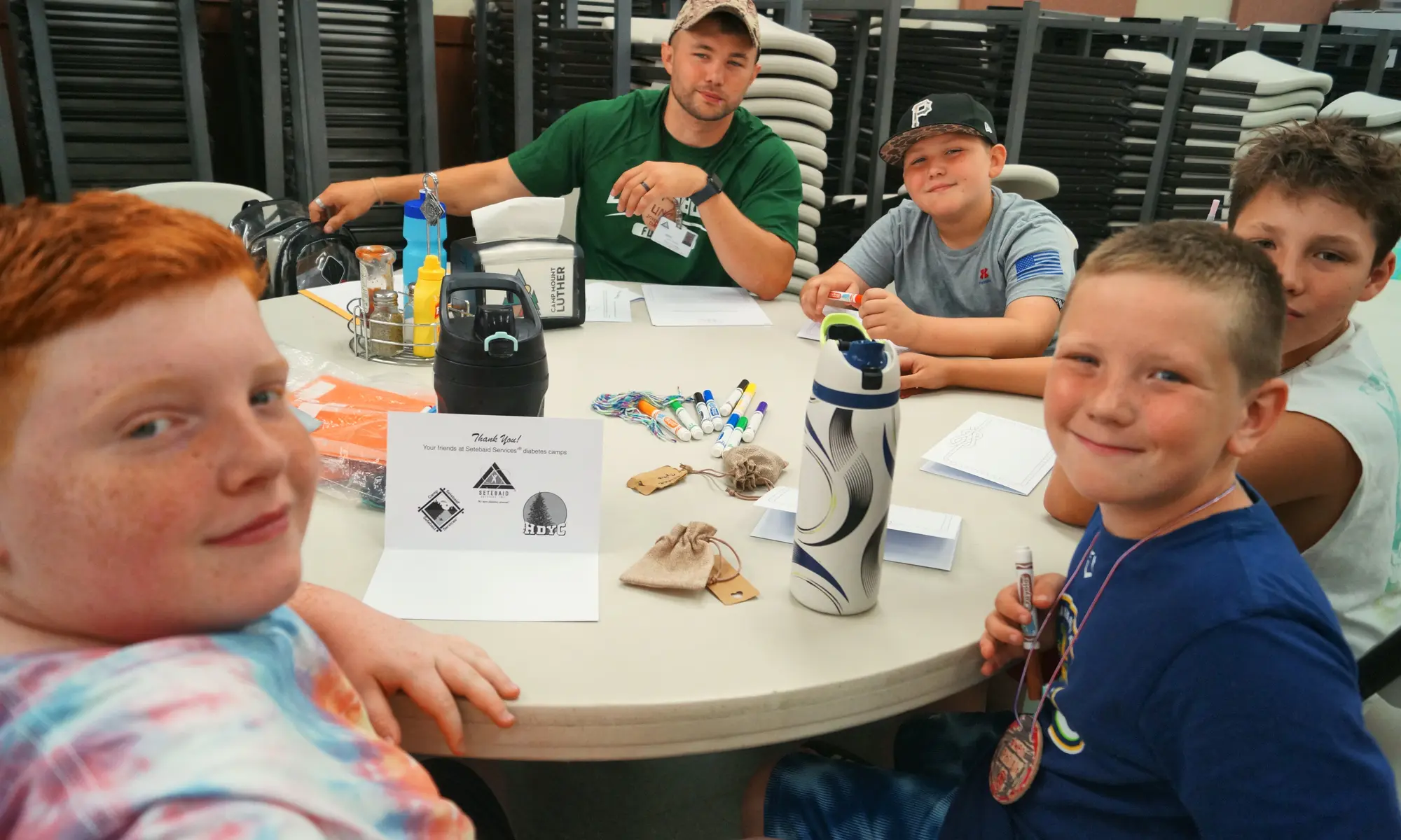 A counselor and a group of smiling boys sit around a table at camp.