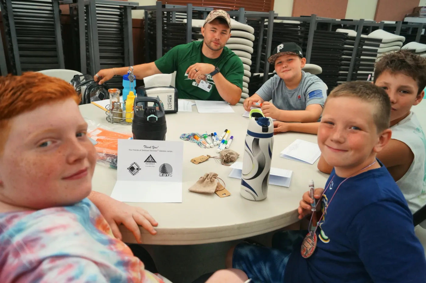 A counselor sits at a table with a group of smiling boys.