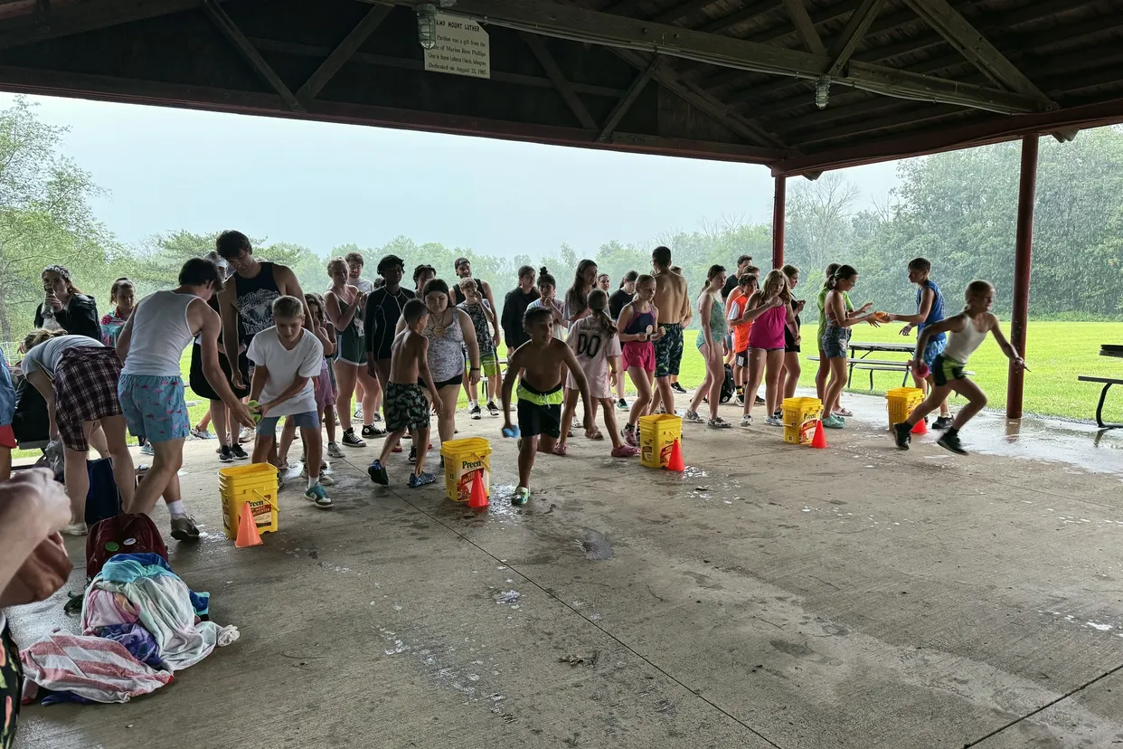 Campers run a water bucket relay race under the covered pavilion