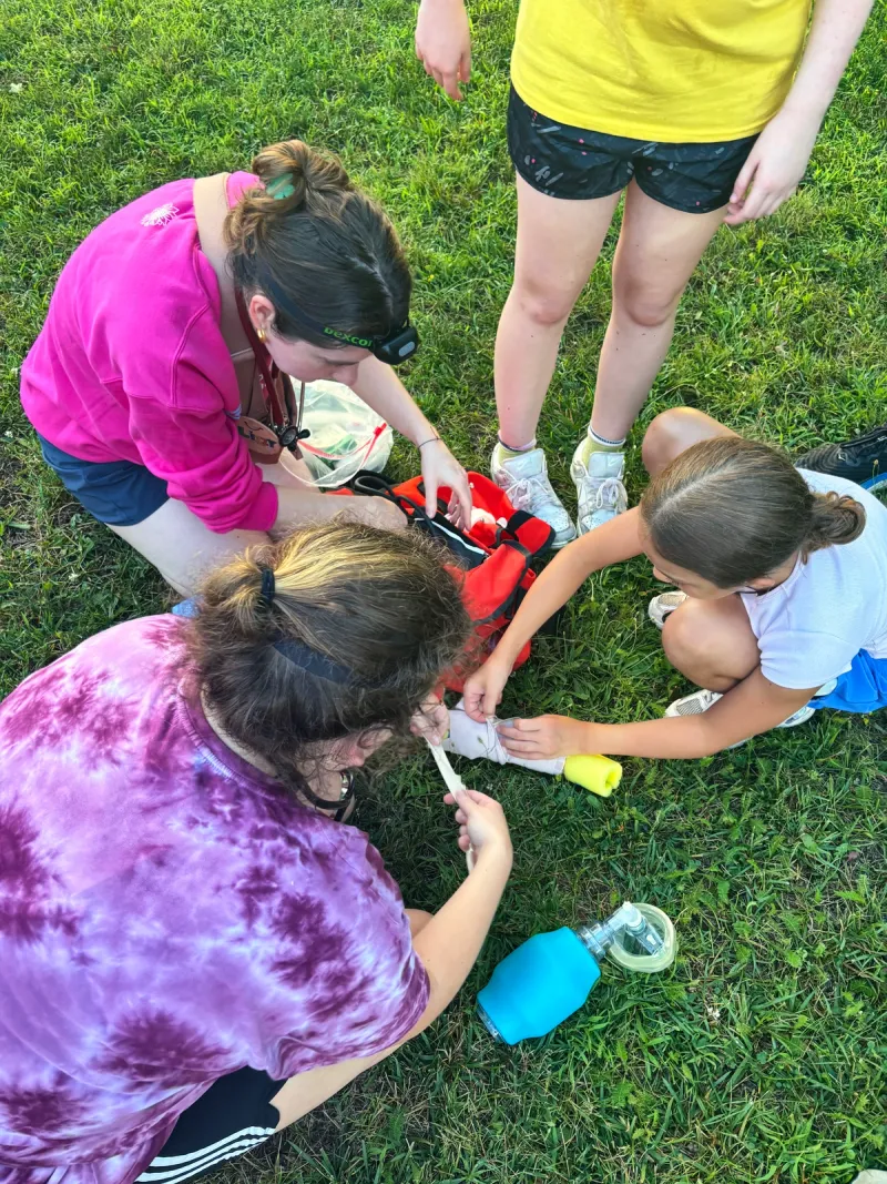 Staff members kneel on the grass and practice first aid with a medical kit.