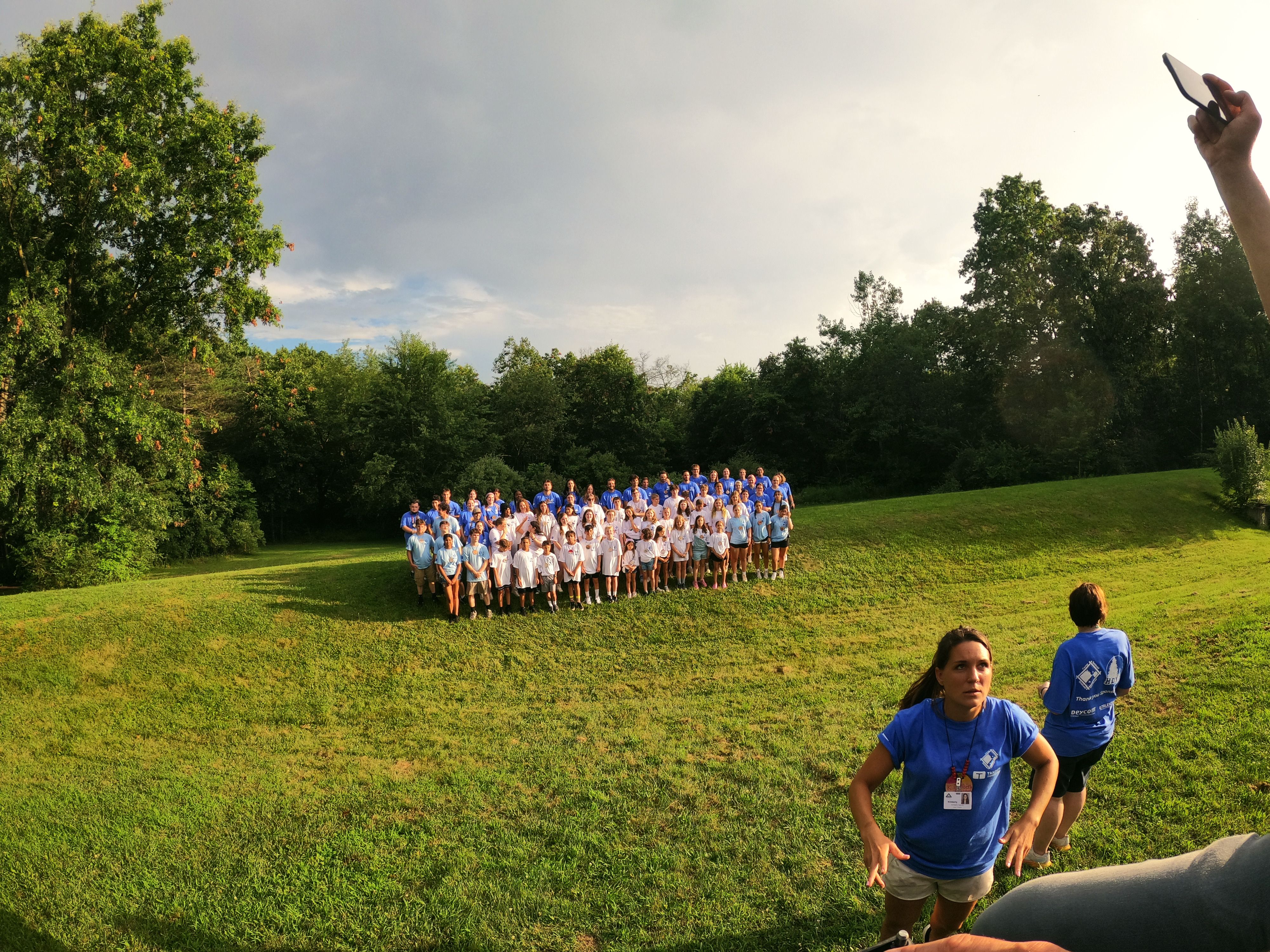 Campers and staff pose for a large group photo on a grassy hill at camp