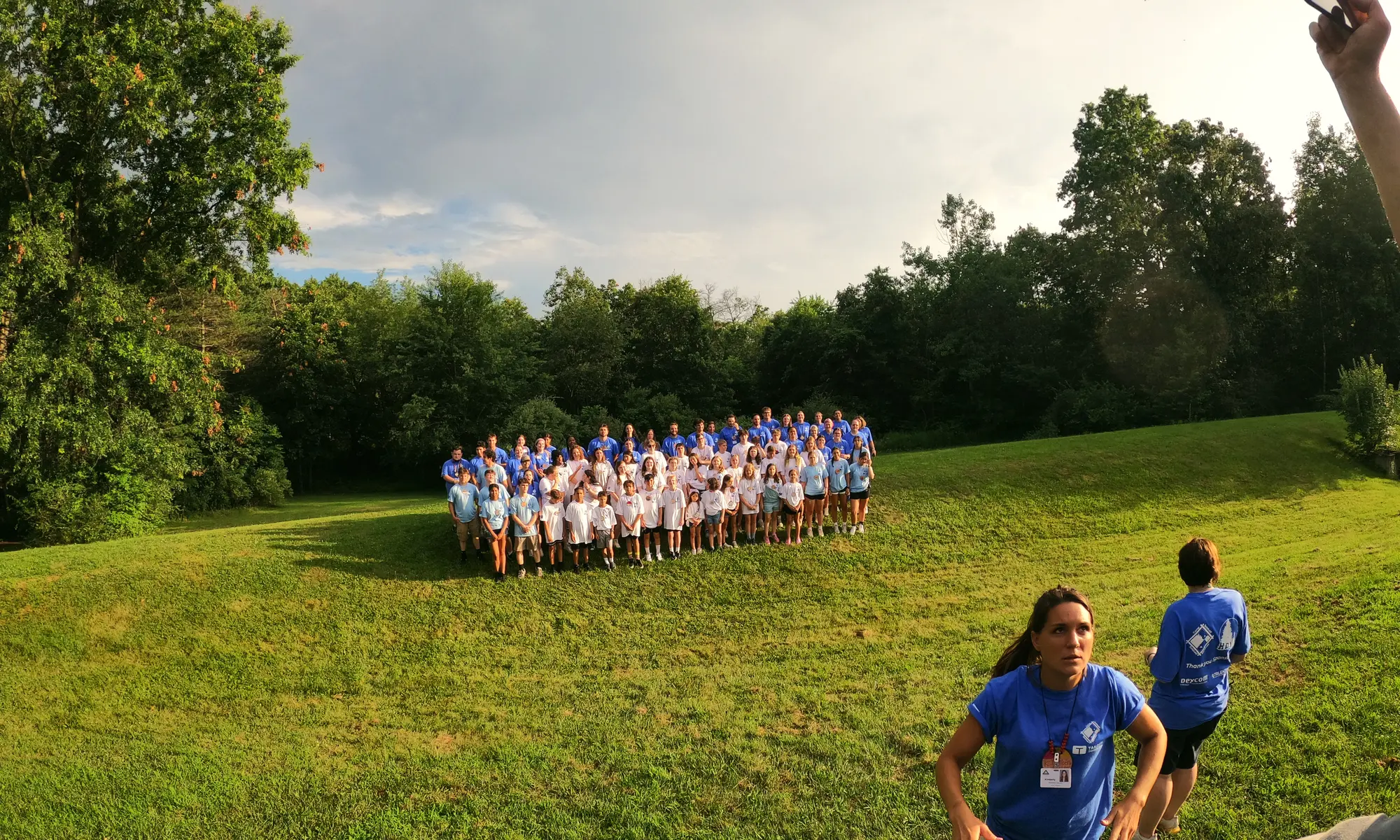 Campers and staff pose for a large group photo on a grassy hill at camp